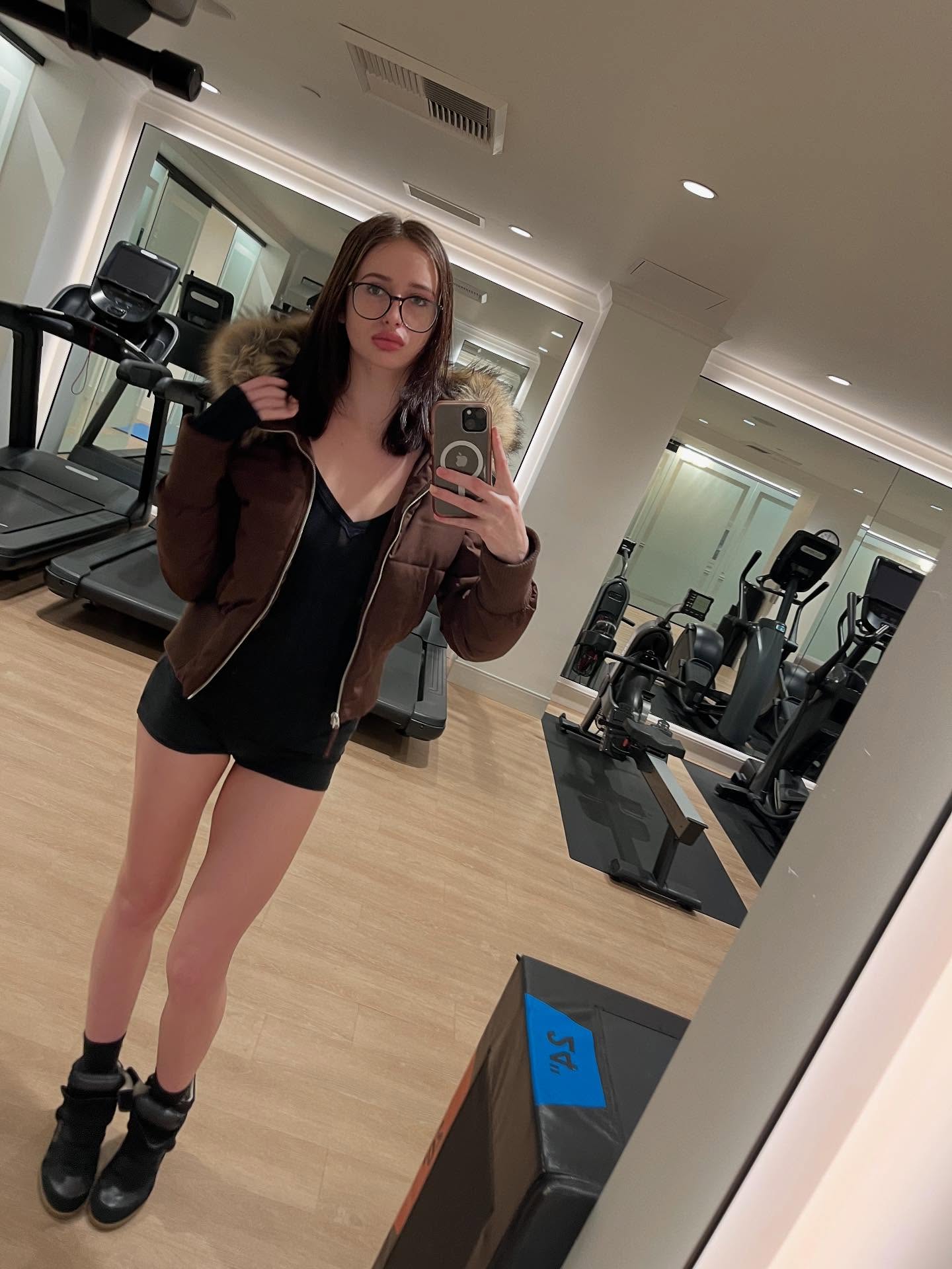 alyssapearls taking a mirror selfie wearing brown puffer jacket in gym