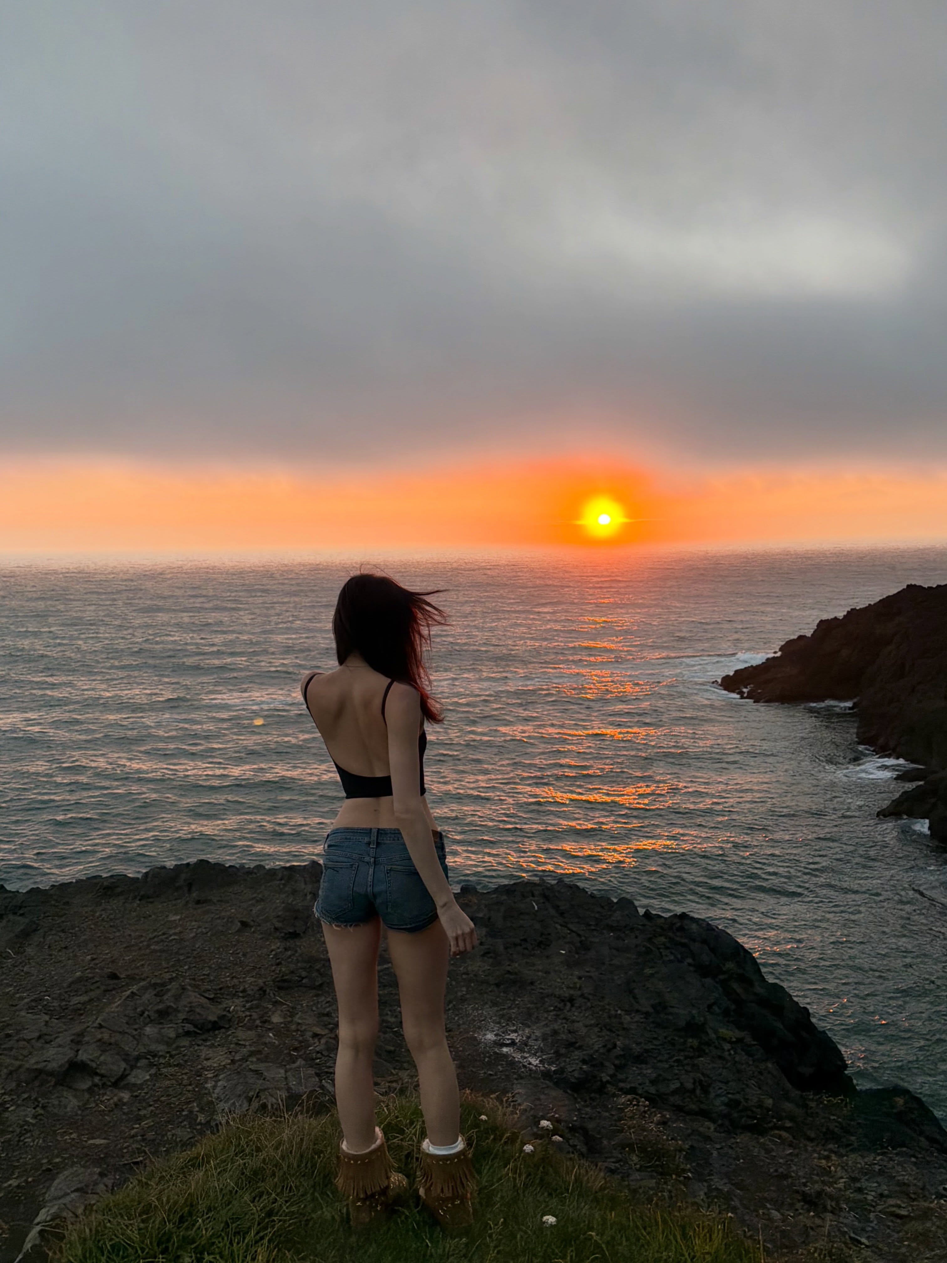 alyssapearls standing looking at sea wearing black backless top in coastal cliff