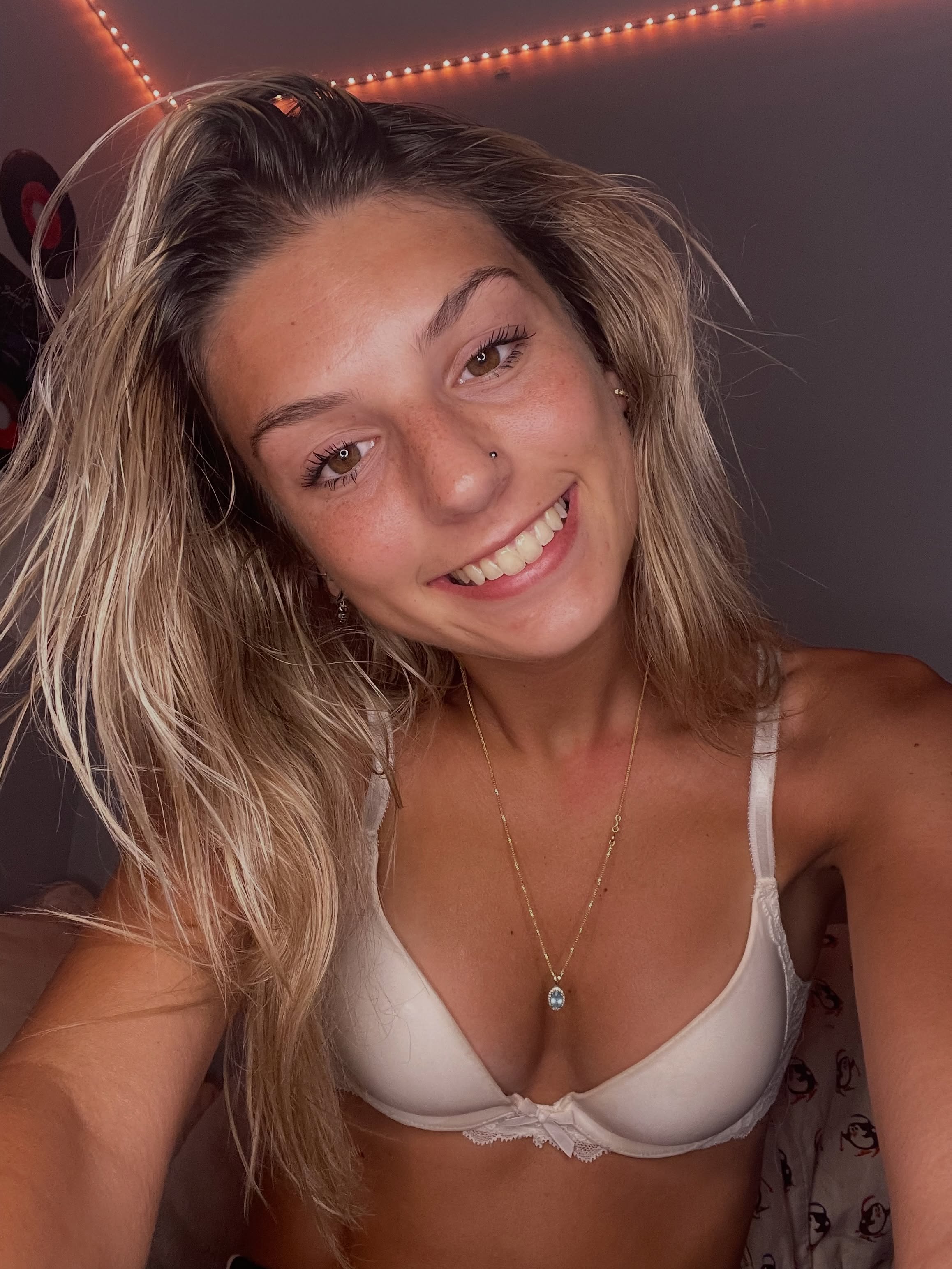 ambiebambiii smiling towards the camera wearing white or cream lace-trimmed bra in bedroom