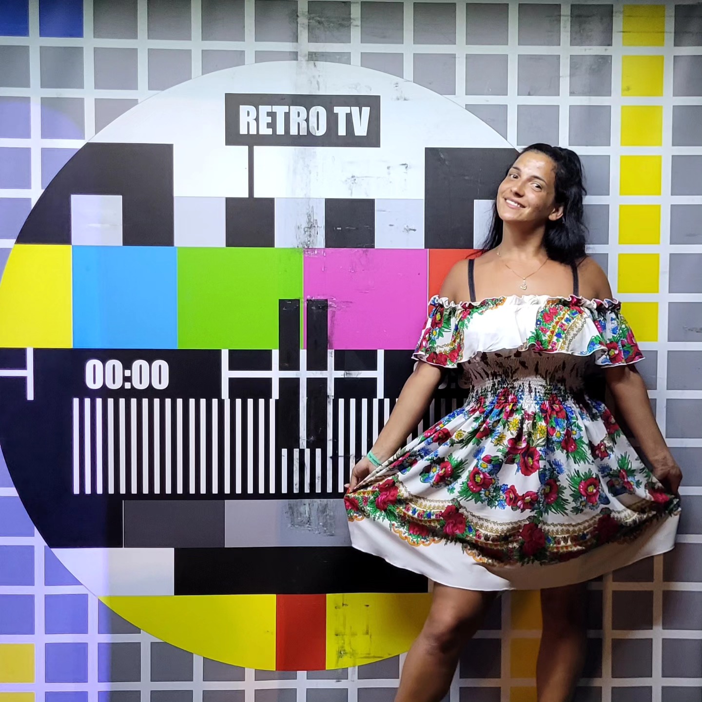 anaworld69 holding out the skirt of her dress wearing white off-shoulder floral dress in front of test pattern backdrop