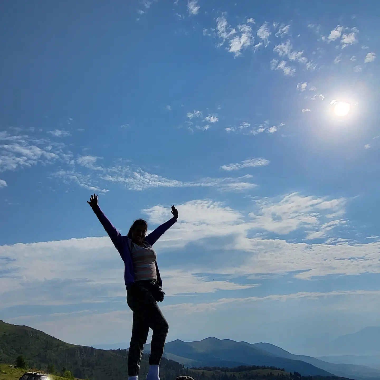 anaworld69 standing with arms raised wearing purple jacket in mountain summit
