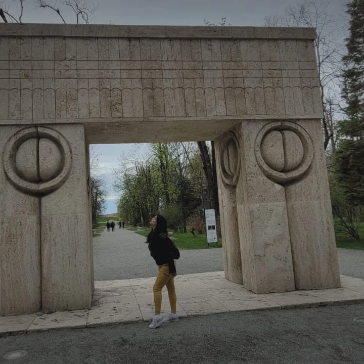 anaworld69 posing under stone arch wearing black jacket in public park at Gate of the Kiss