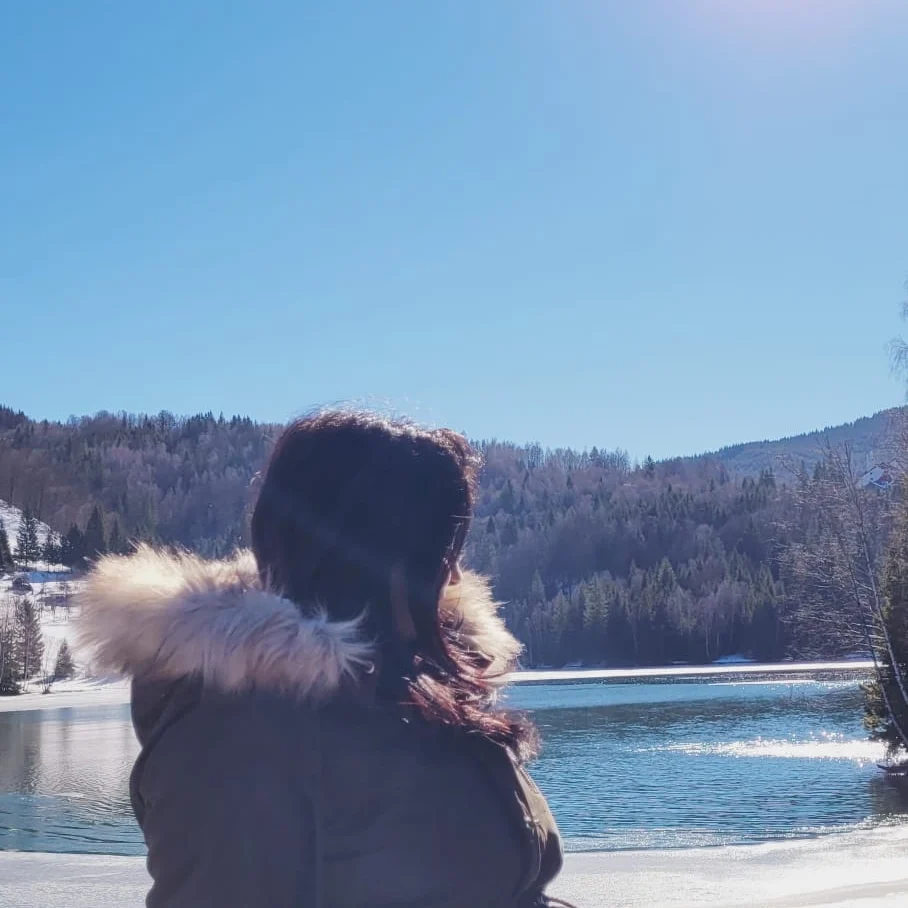 anaworld69 standing outside wearing dark winter jacket with fur hood in mountain lake
