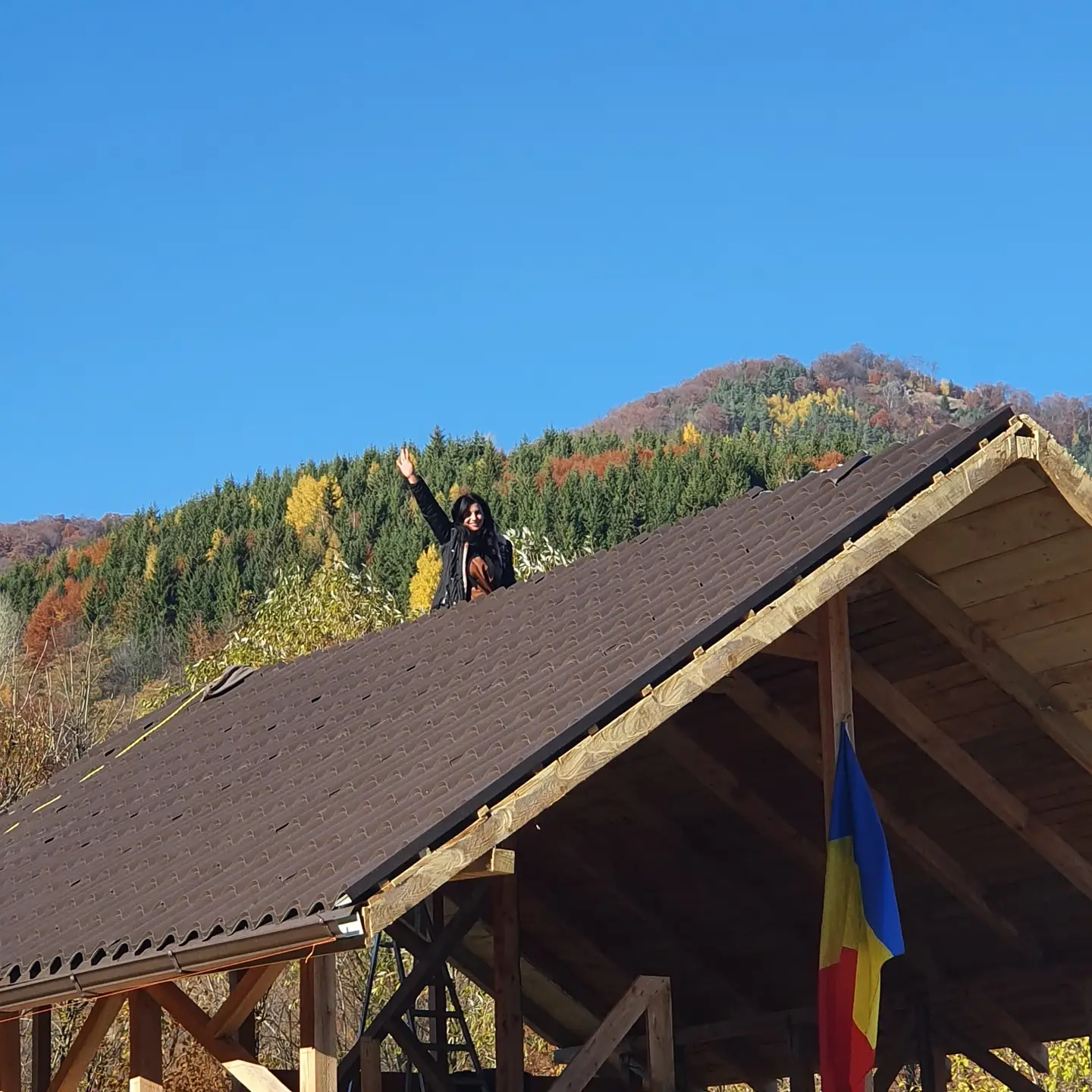 anaworld69 waving hand from roof wearing black jacket in mountainous rural area