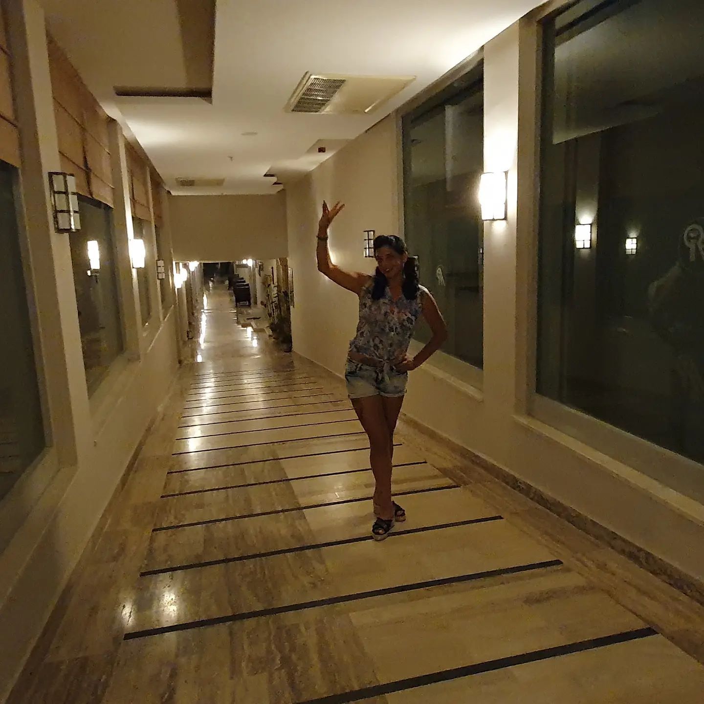 anaworld69 posing with arm raised wearing patterned sleeveless top in hallway