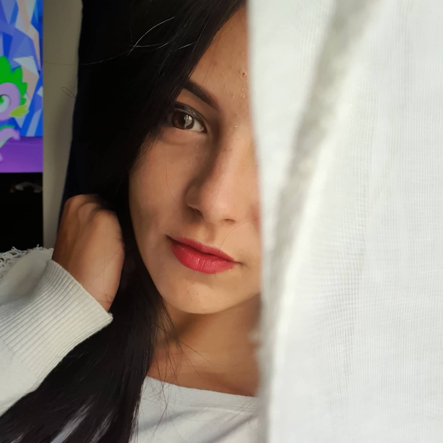 anaworld69 peeking behind a curtain wearing white long-sleeved top