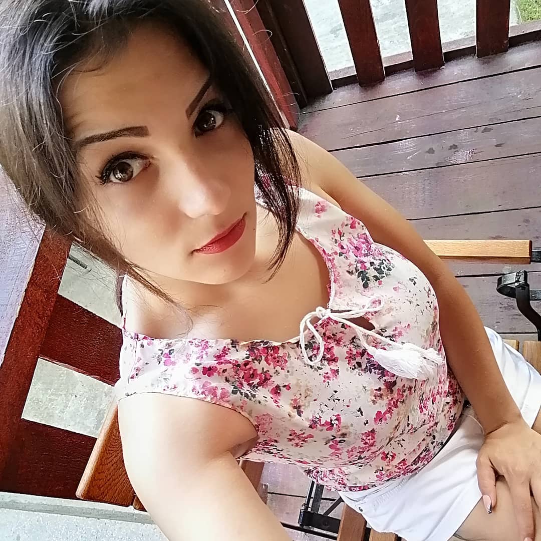 anaworld69 sitting on a chair wearing pink floral top in wooden porch