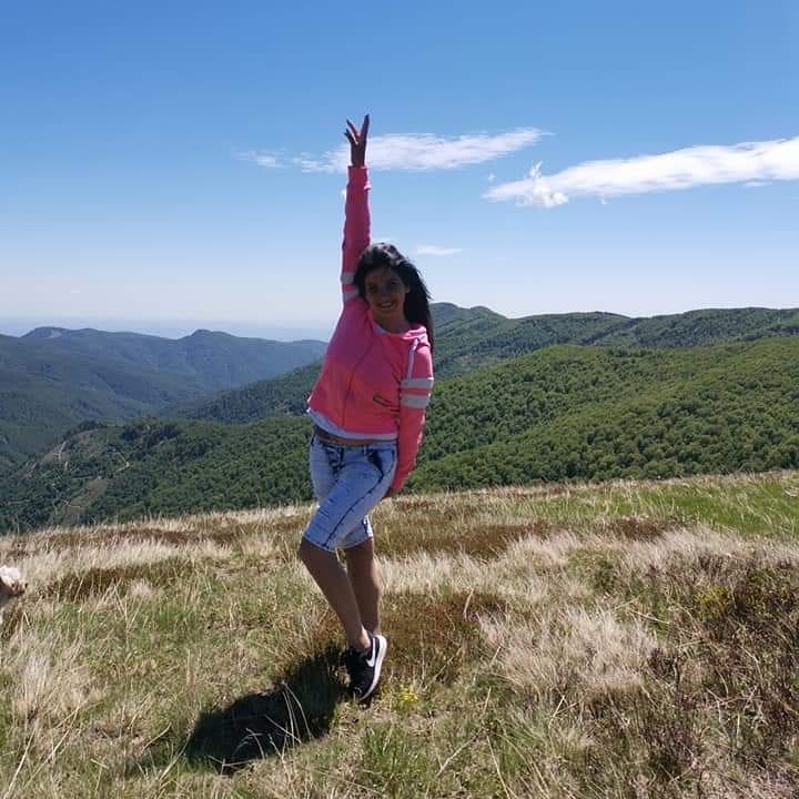anaworld69 posing with arm raised wearing pink zip-up hoodie in mountain summit
