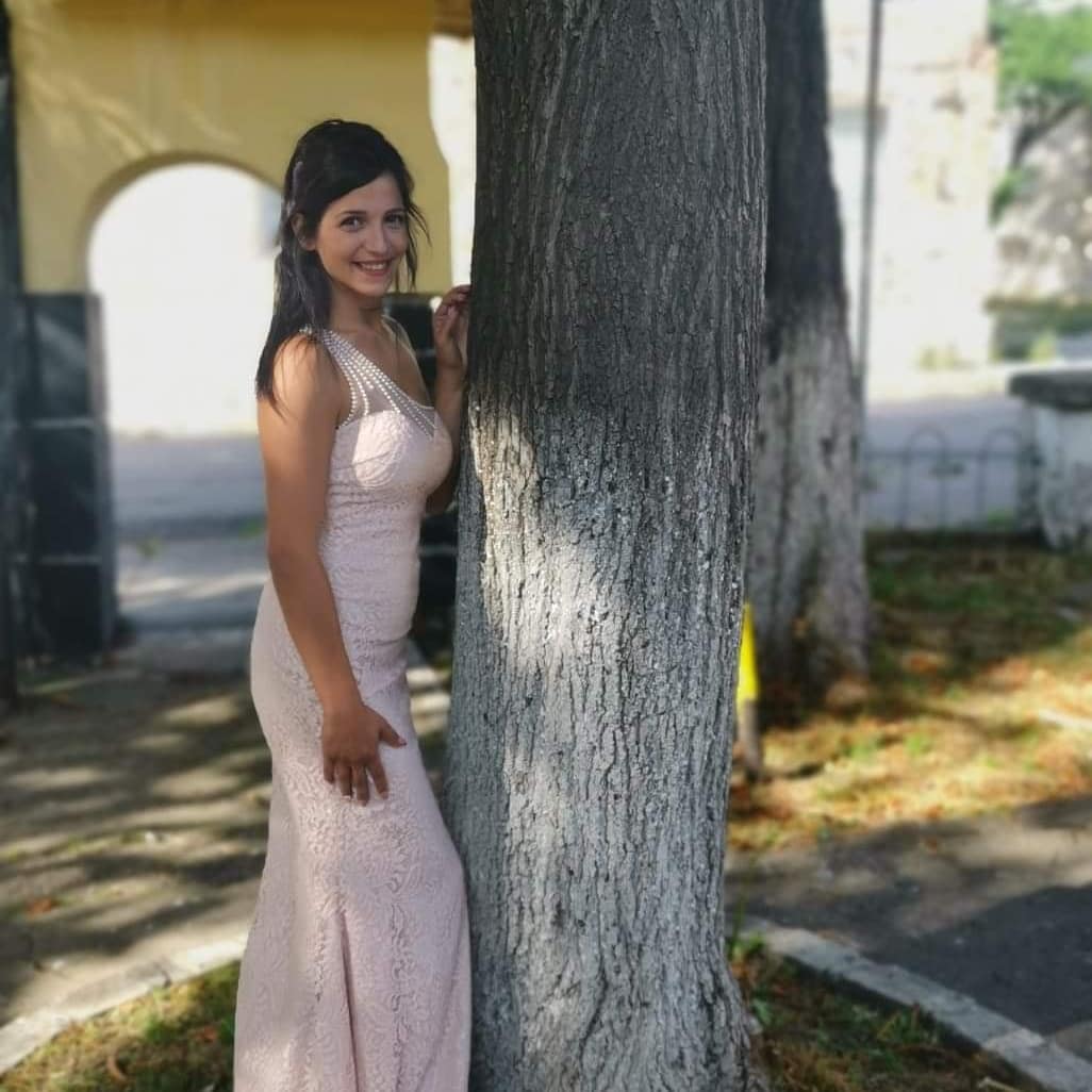 anaworld69 leaning against a tree wearing light pink sleeveless lace dress near trees