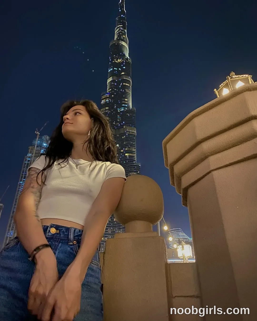 Alice Standing beside the balustrade wearing White short-sleeved cropped T-shirt beside a stone balustrade