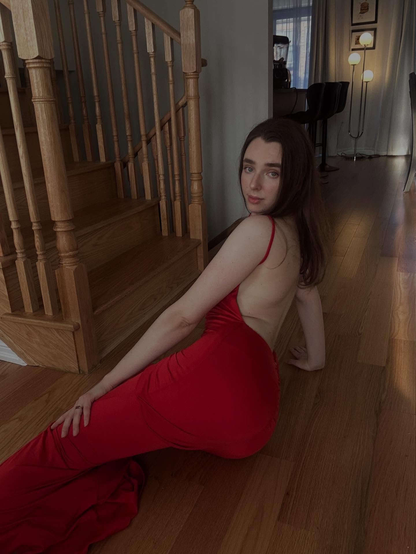 annabisoux sitting on the floor wearing red backless dress in hallway near stairs