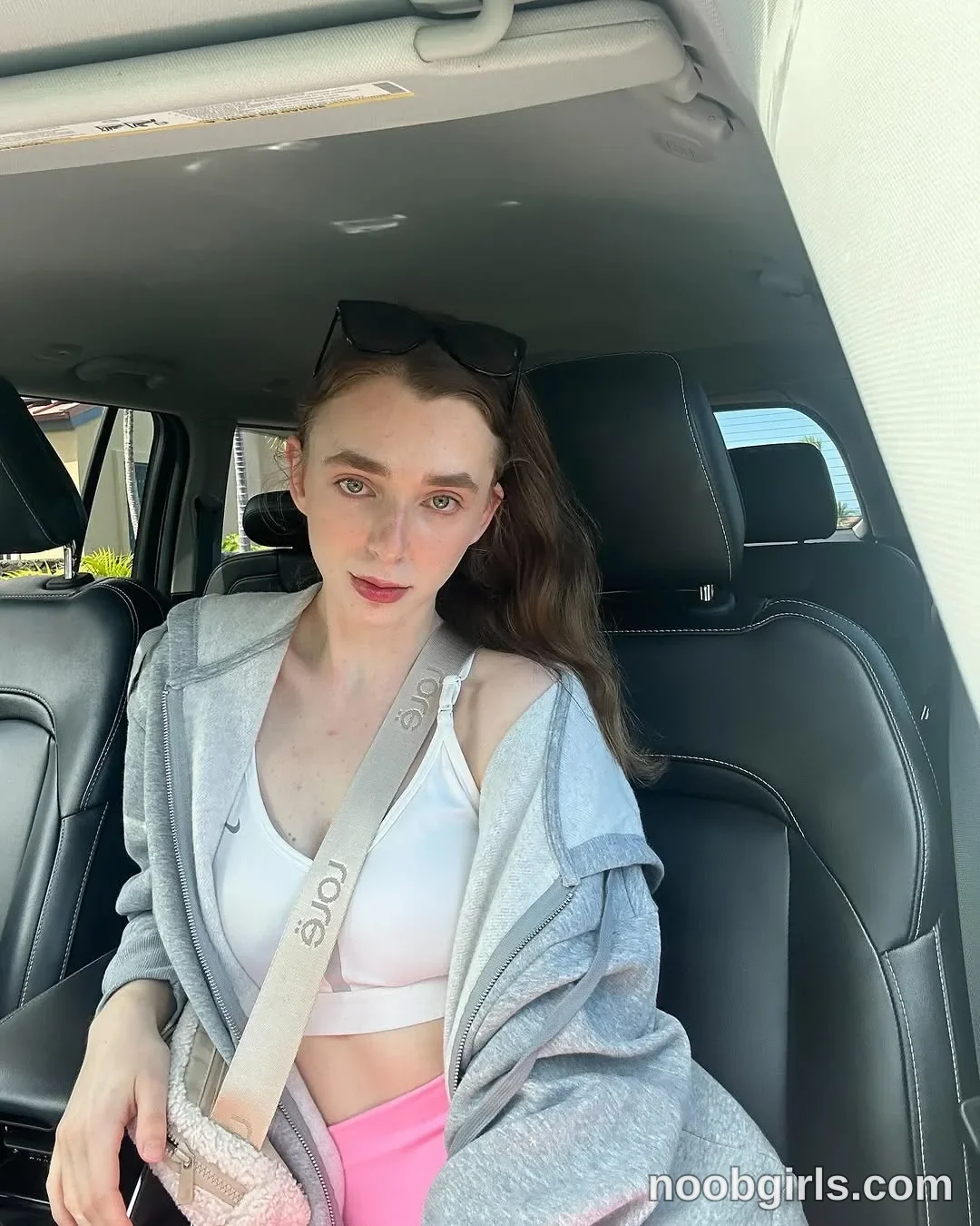 Anna sitting in the passenger seat of a vehicle looking towards the camera wearing grey zip-up hooded jacket