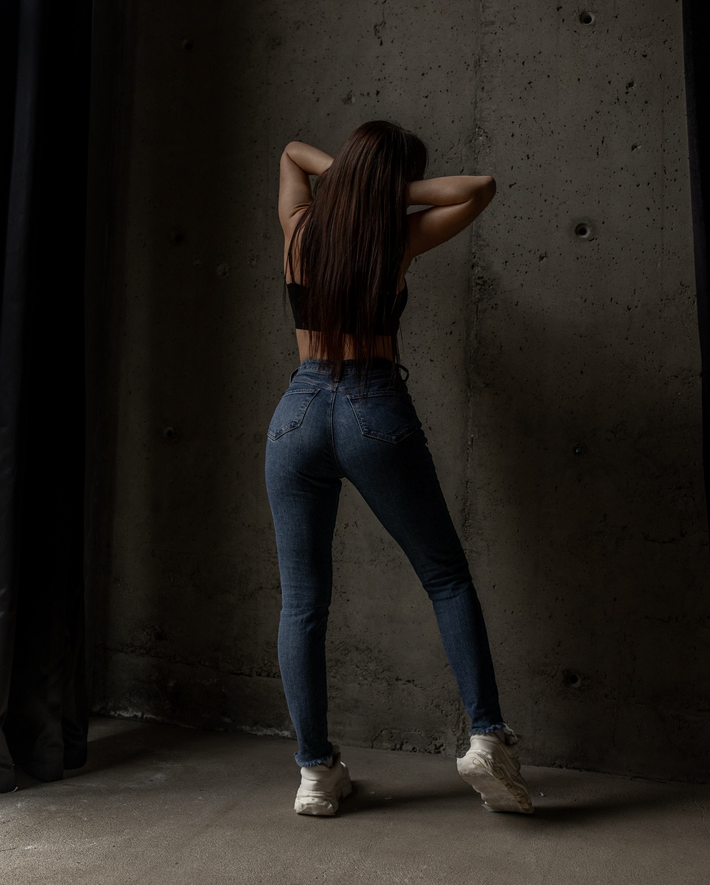 anny54784 posing with hands behind head wearing black crop top in concrete wall interior