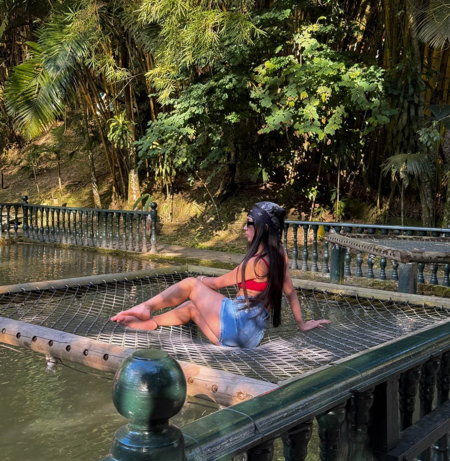 ashley_jones9 reclining on a net over water wearing red bikini top in pond in tropical garden