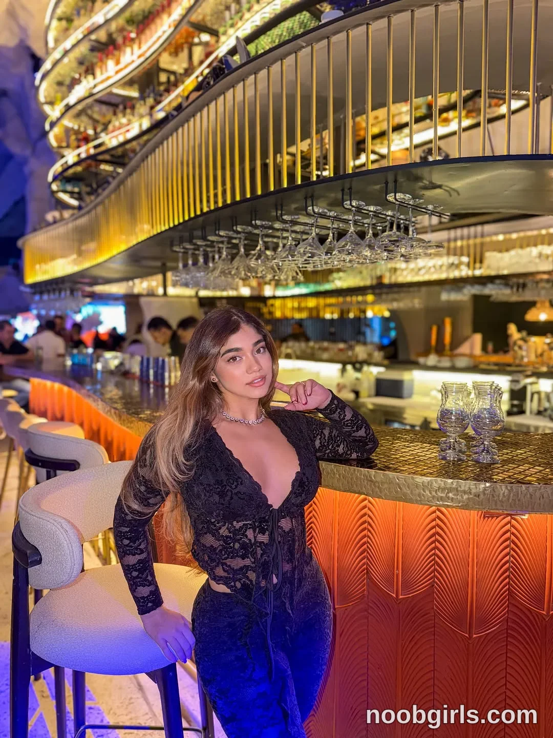 Ale sitting on a bar stool wearing black sheer lace long-sleeved top with plunging neckline and front tie closure