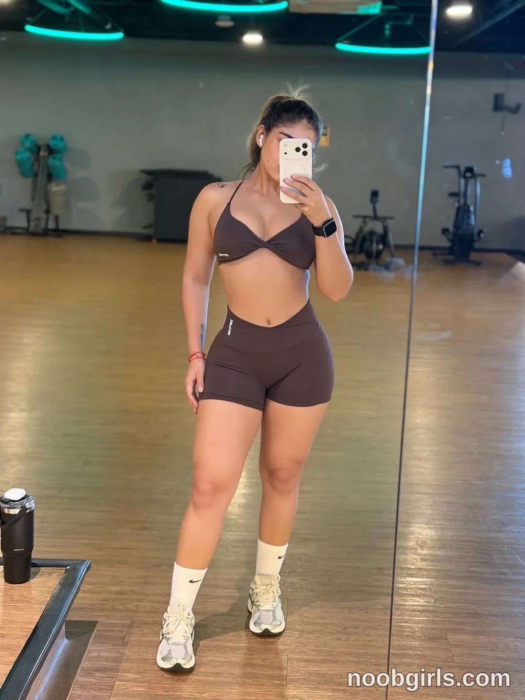 Ale taking a mirror selfie wearing dark brown sports bra / bikini-style athletic top in gym or fitness studio
