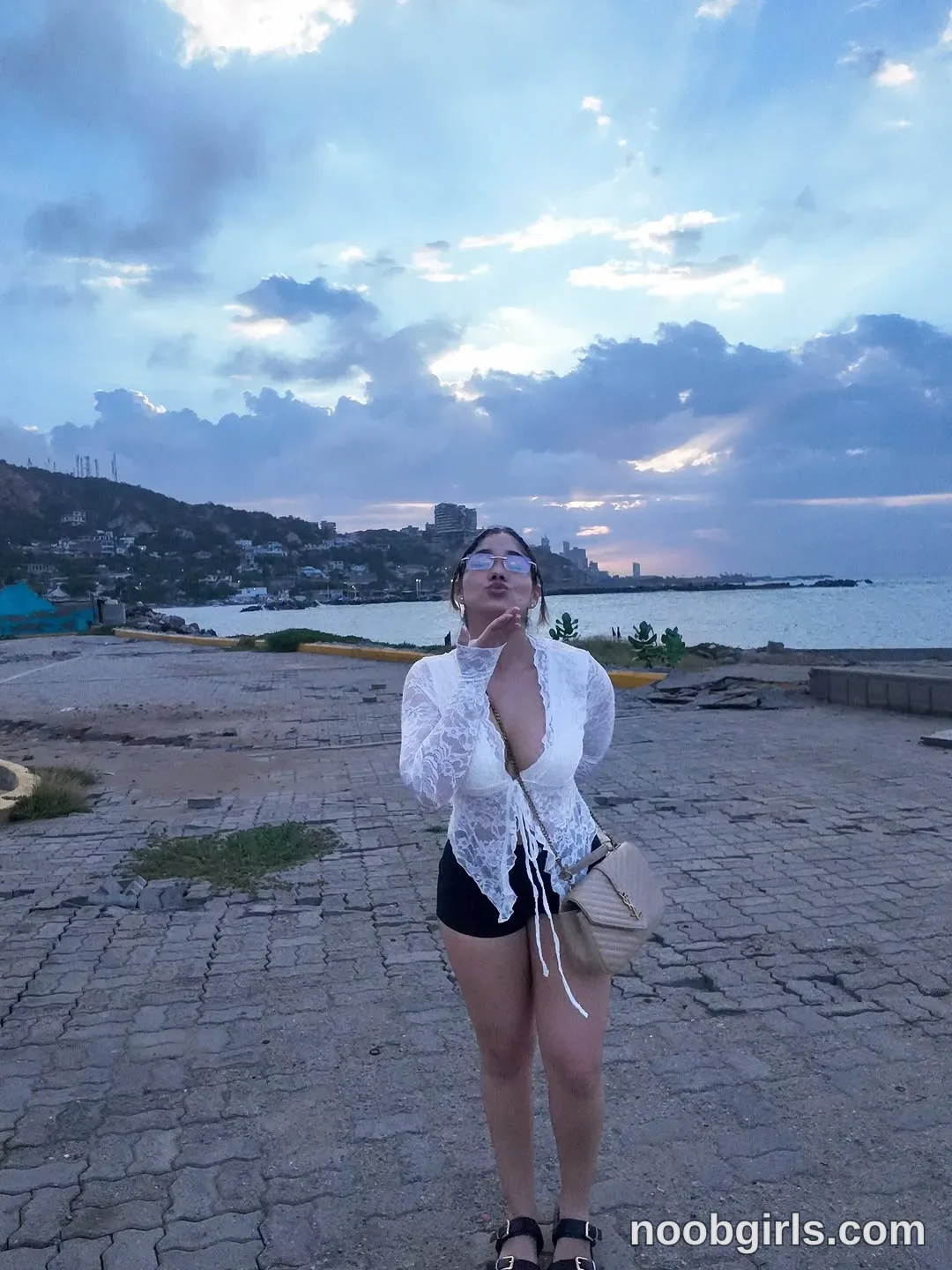 Ale standing on paved ground wearing white long-sleeve lace top with tie front