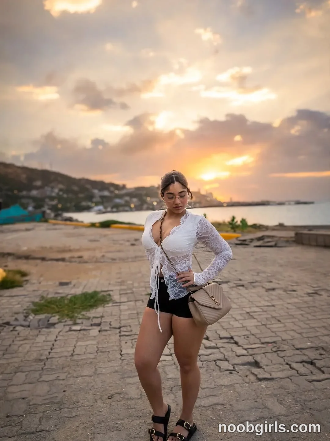 Ale standing on paved ground with one hand on hip wearing white long-sleeved sheer lace tie-front top