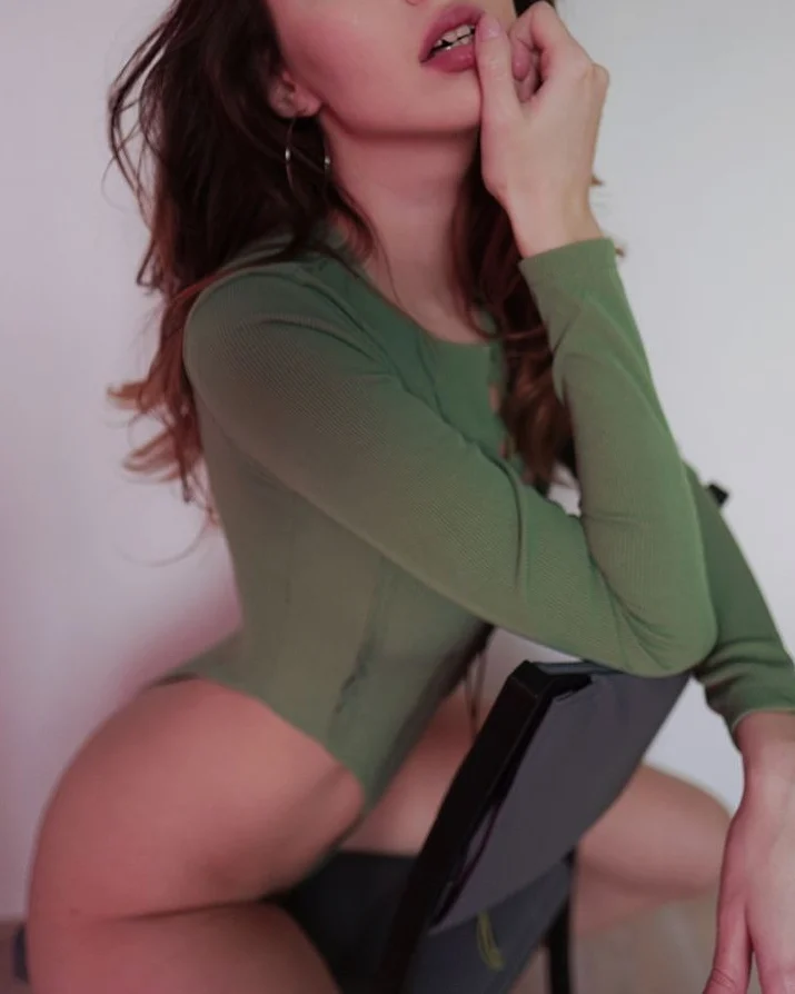 asuna_niiya posing on chair wearing green long-sleeve bodysuit in room