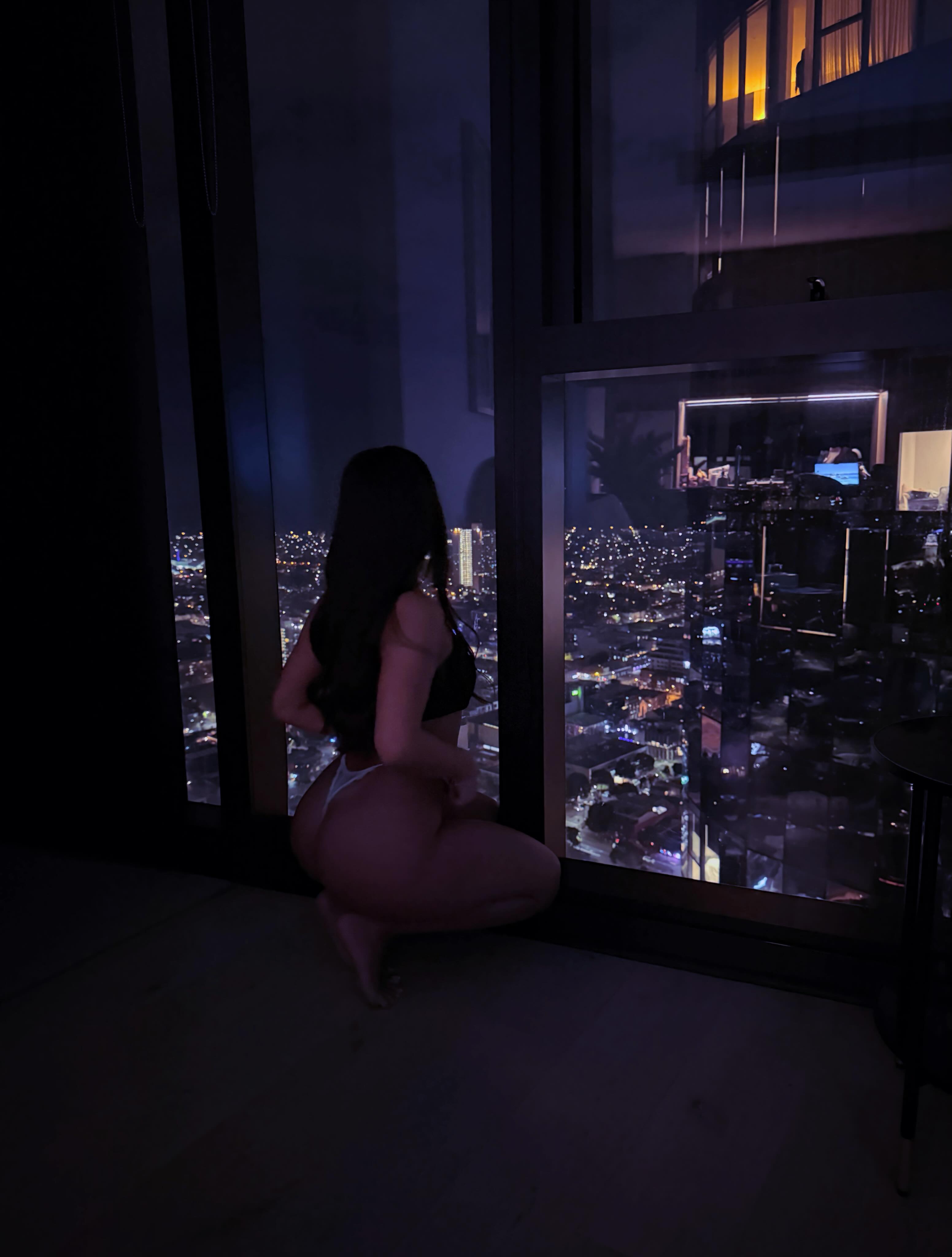 ava_delightt crouching looking outside wearing black top in high-rise room at night
