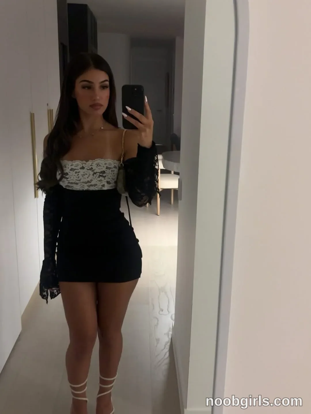 Ava Standing in front of a mirror wearing Short black dress with a white lace bodice panel and long black lace sleeves