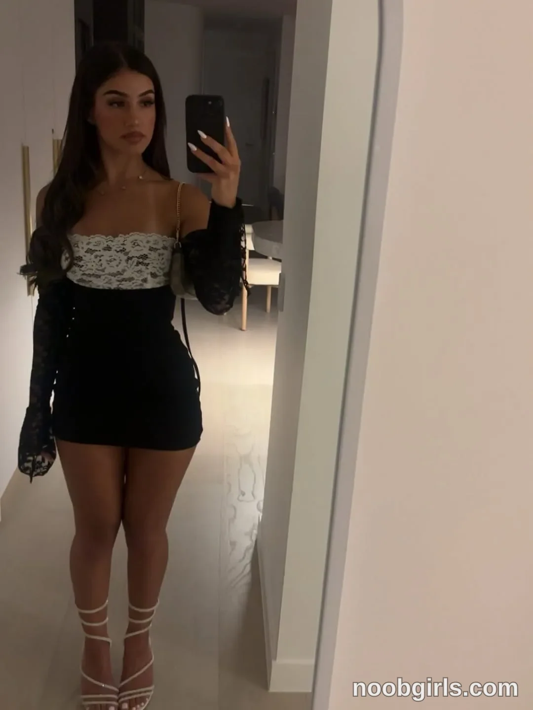 Ava Standing in front of a mirror wearing Black mini dress with a white lace bust panel and long black lace sleeves