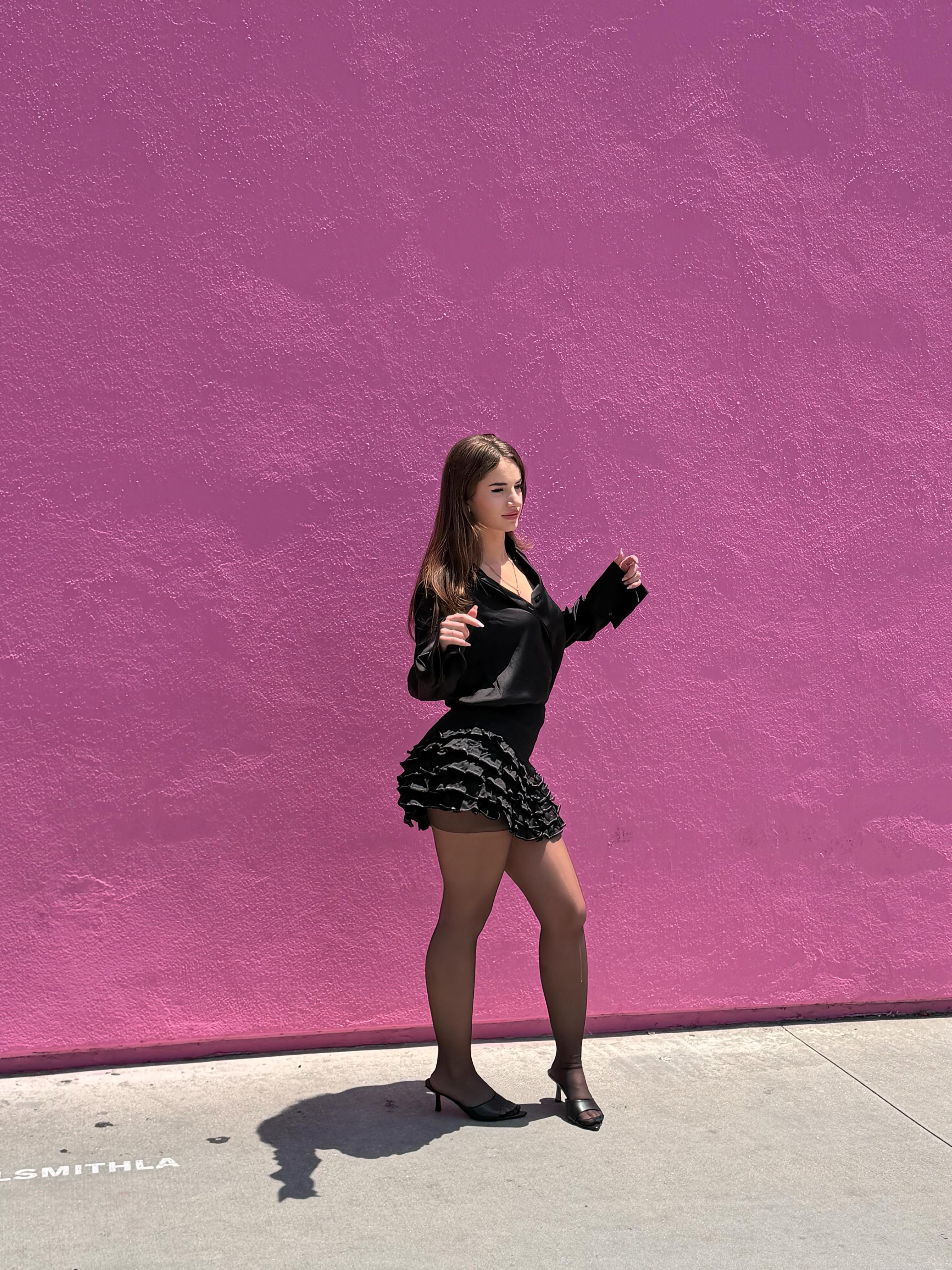 aviebby wearing black long-sleeve top in sidewalk by pink wall at Paul Smith Pink Wall, Los Angeles