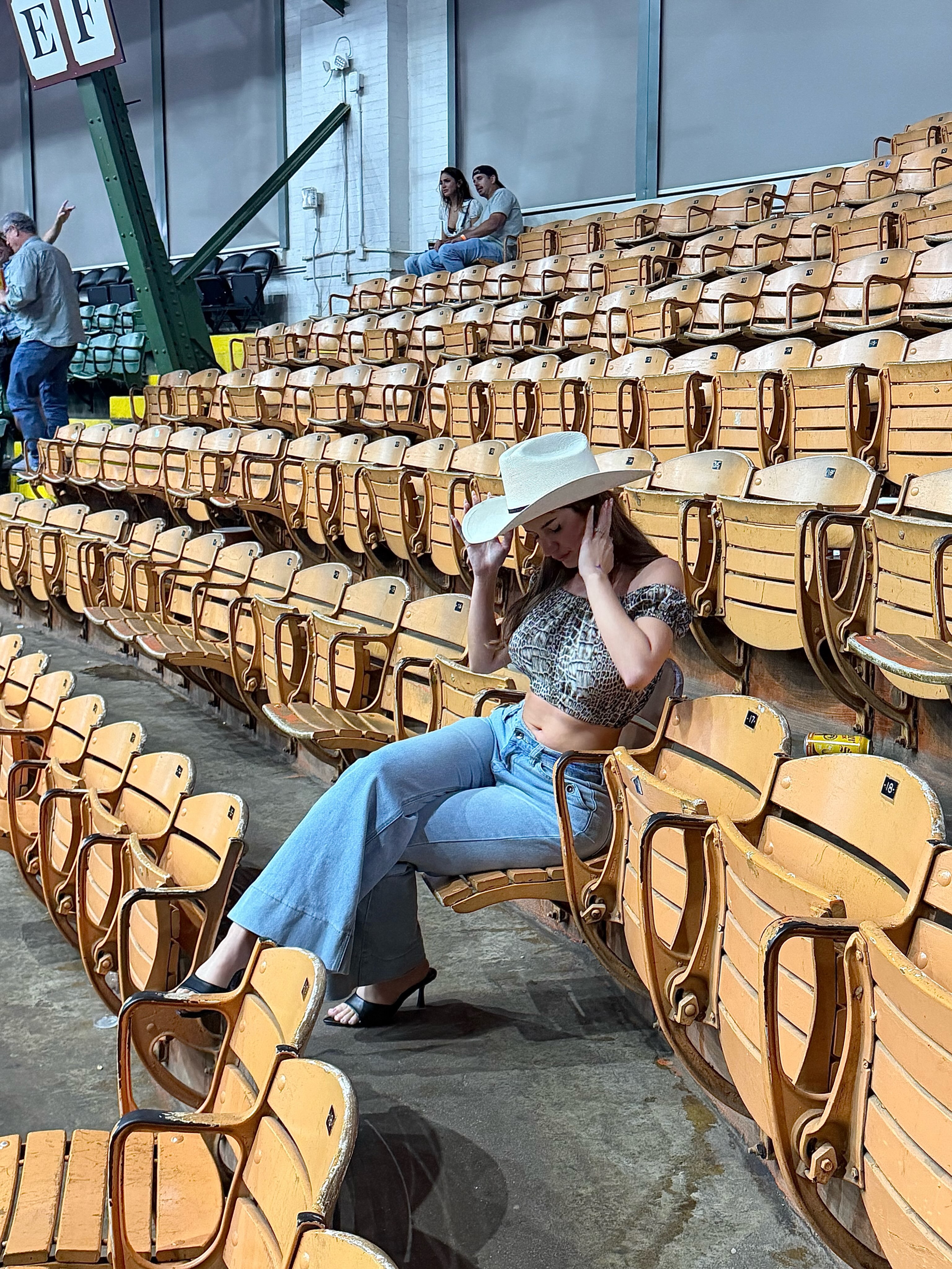 aviebby sitting on wooden stadium seat wearing white cowboy hat in stadium seating area
