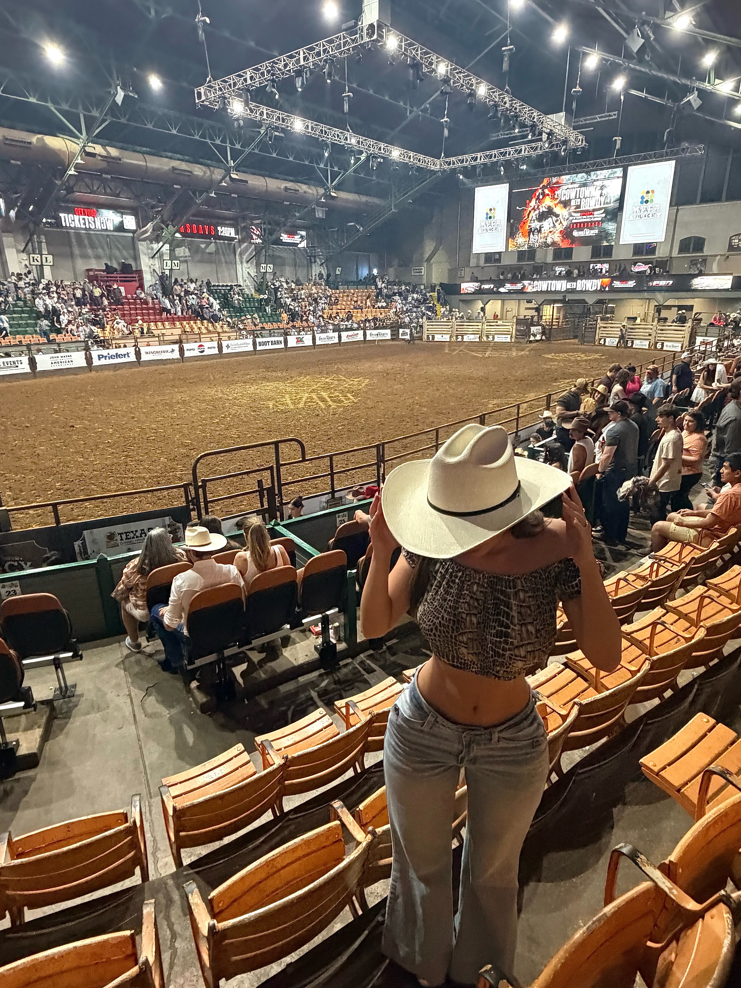 aviebby standing among stadium seats wearing white cowboy hat in rodeo arena at Cowtown Coliseum