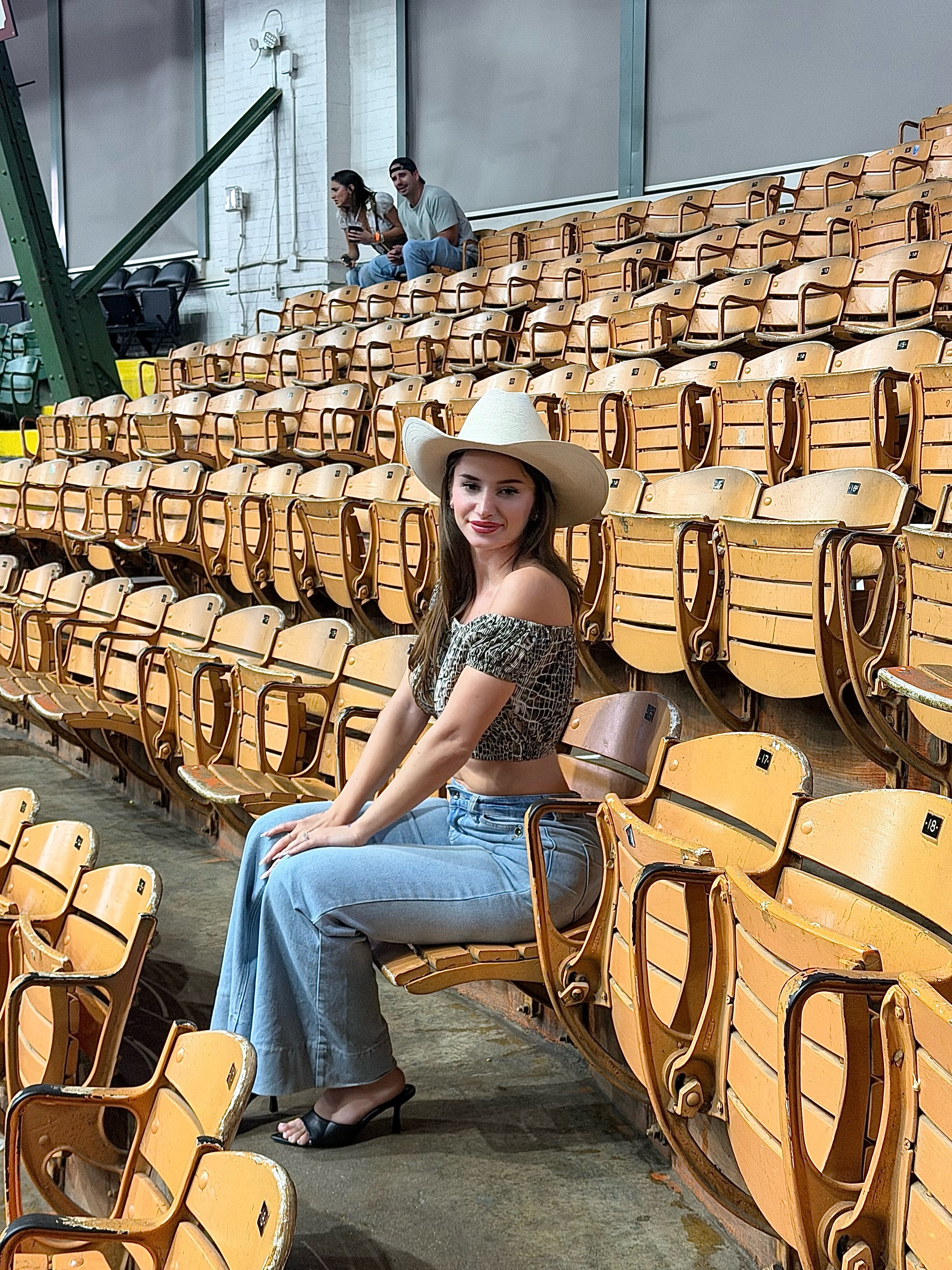 aviebby sitting on wooden stadium seat wearing white cowboy hat in stadium seating area