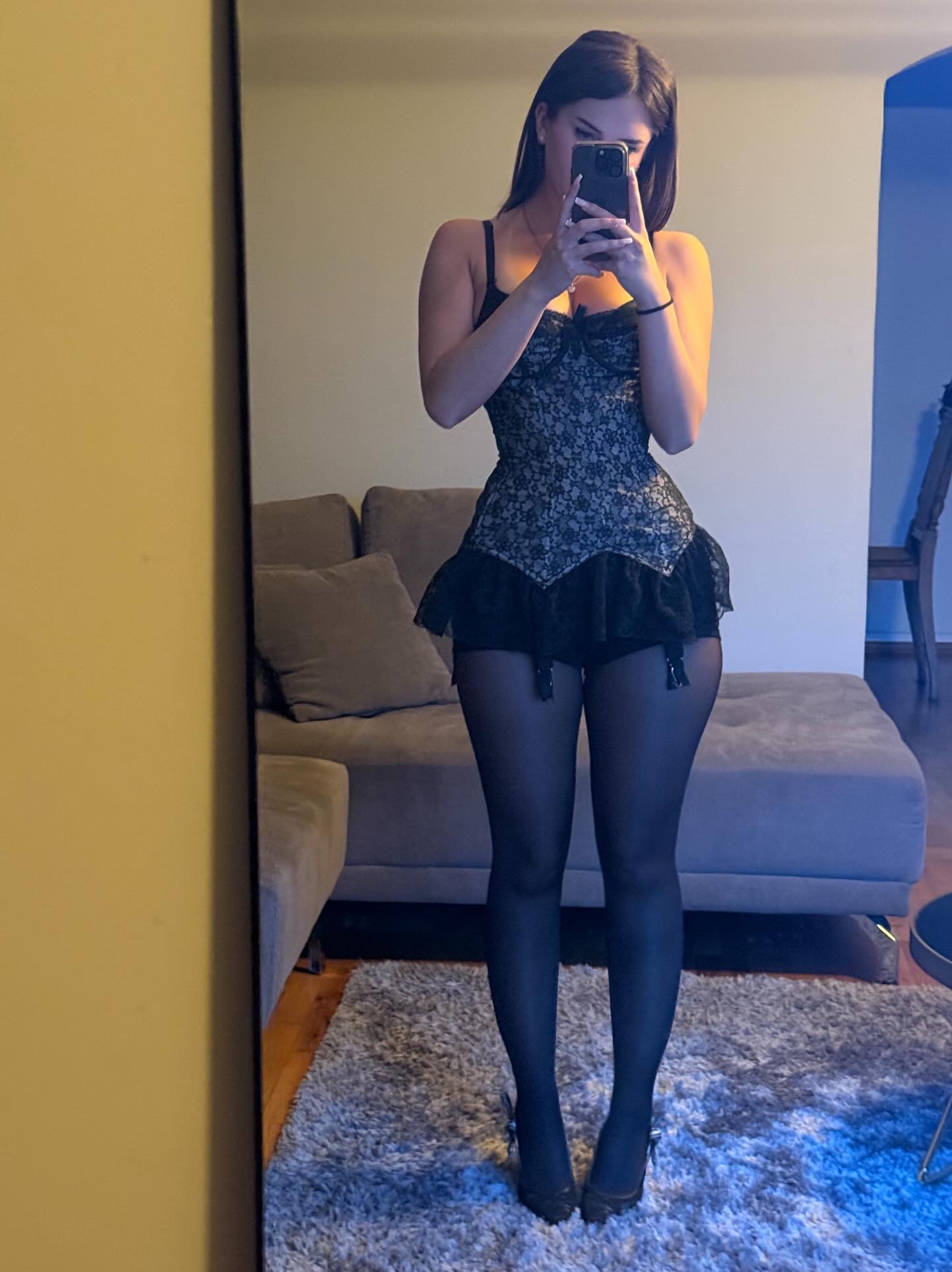aviebby taking a mirror selfie wearing black lace corset top in living room