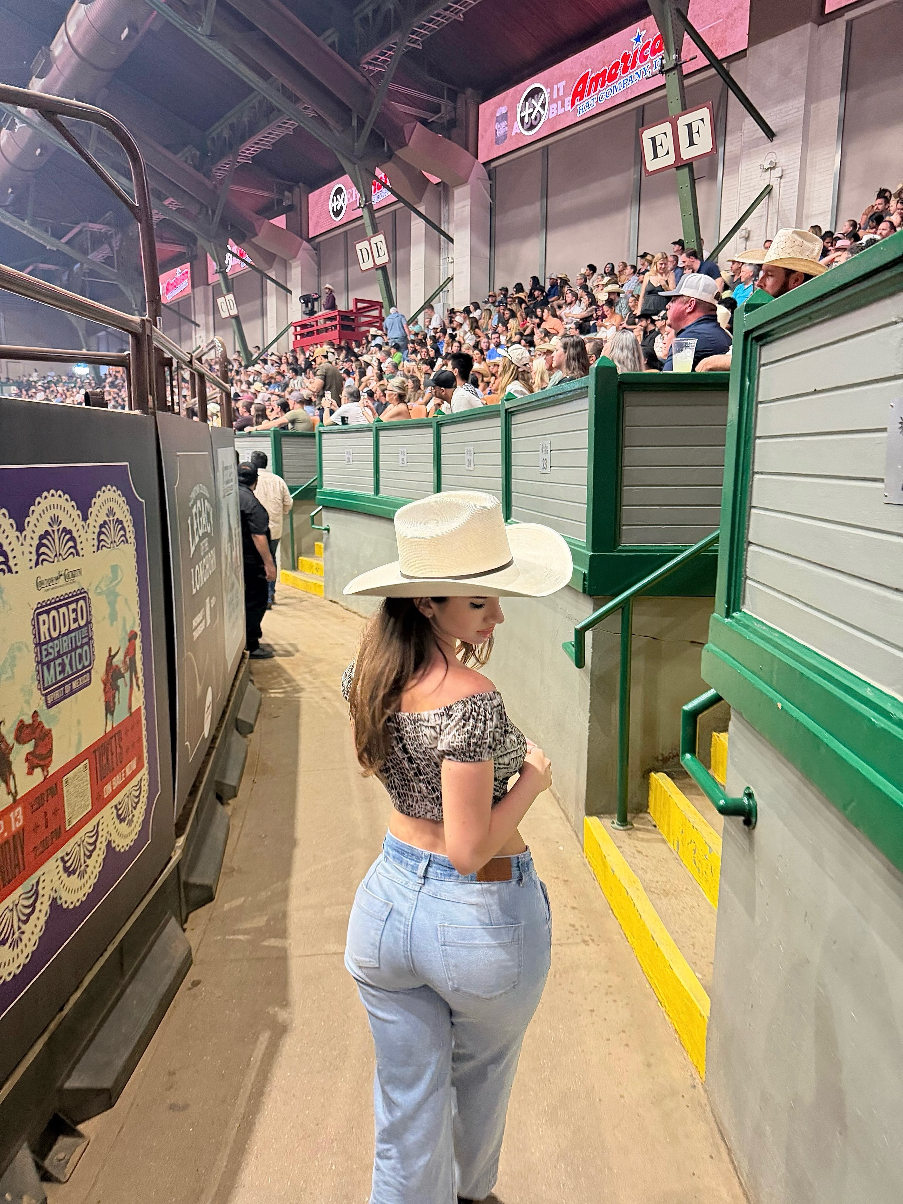 aviebby walking along aisle wearing white cowboy hat in rodeo arena