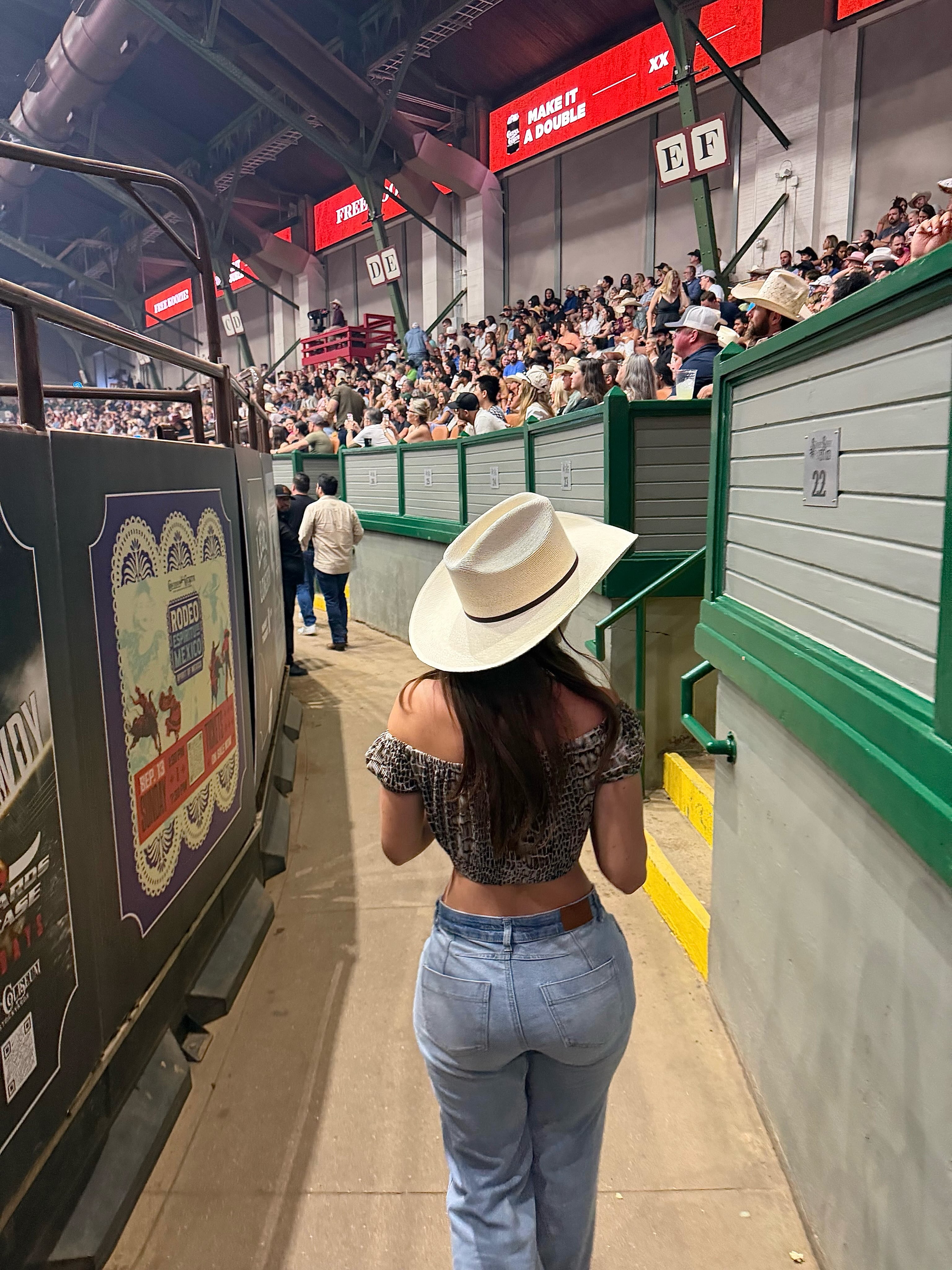 aviebby walking along a walkway wearing white cowboy hat in arena concourse