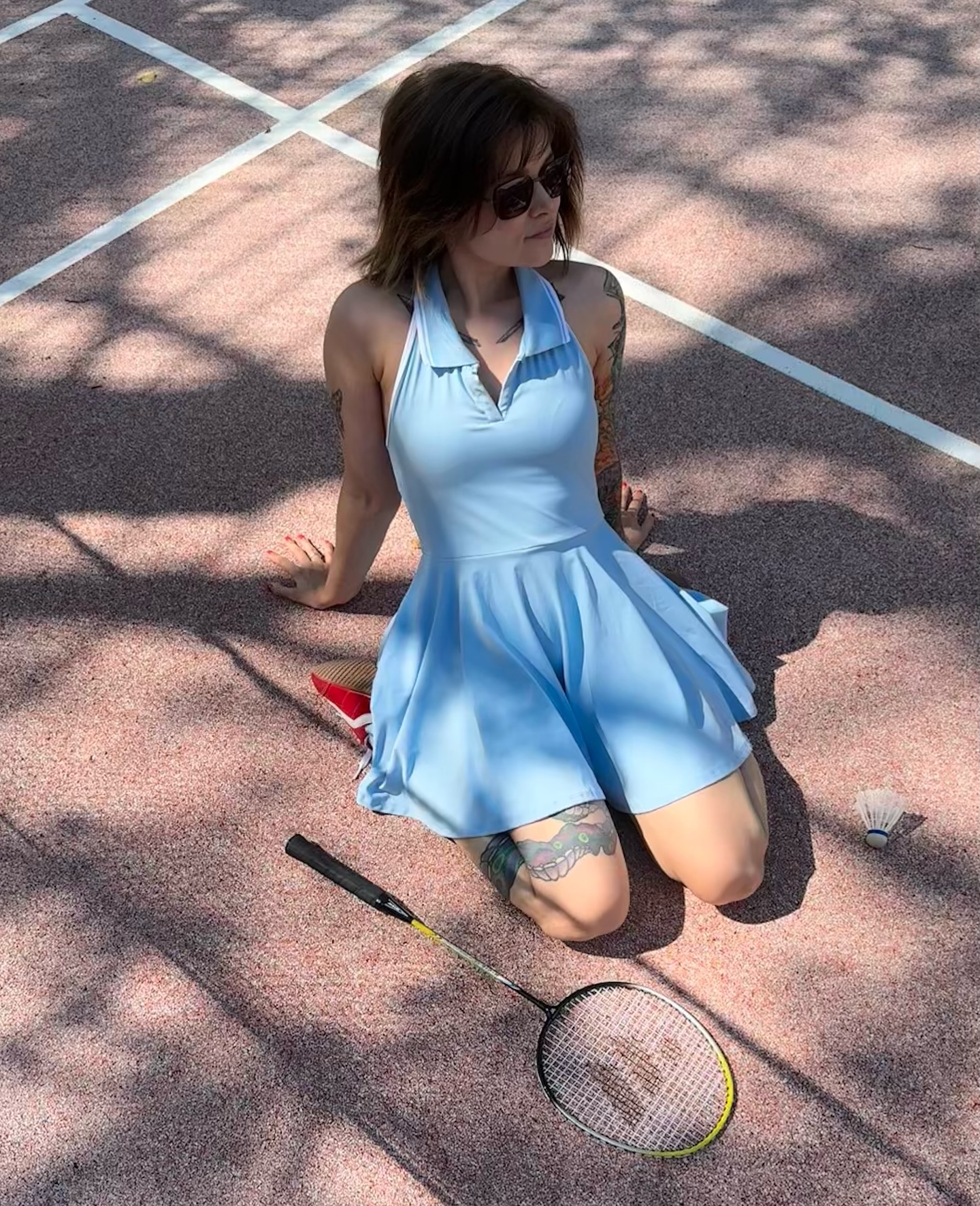 awondrr kneeling on the ground near a racquet wearing light blue tennis dress in badminton court