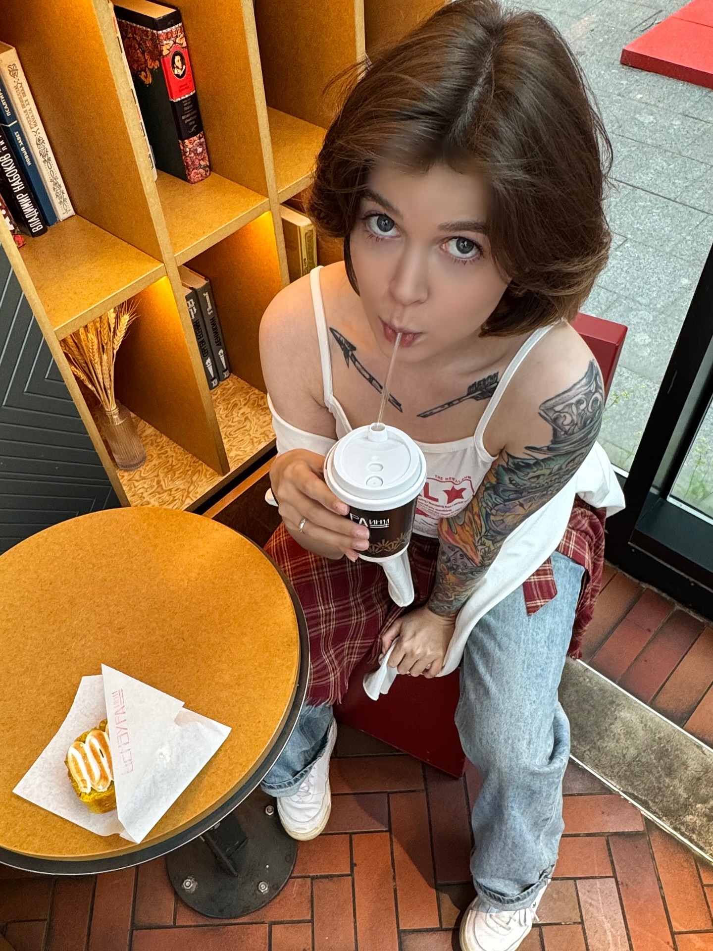 awondrr drinking from a cup with a straw wearing white tank top in cafe