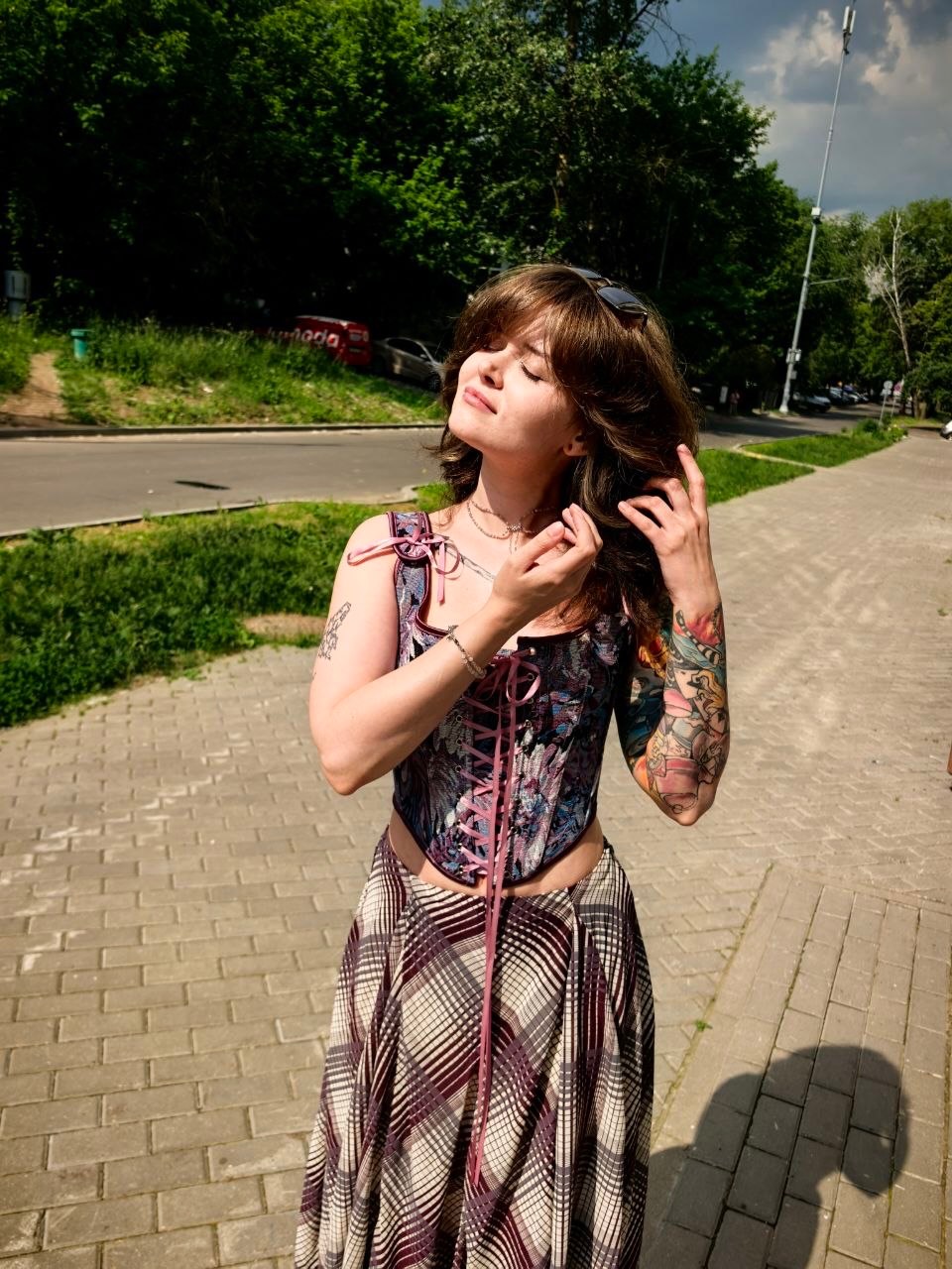 awondrr touching hair with eyes closed wearing patterned lace-up corset top in paved sidewalk near a street