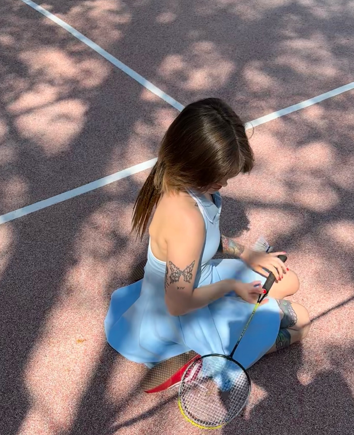 awondrr sitting on the ground holding a badminton racket wearing light blue dress in court