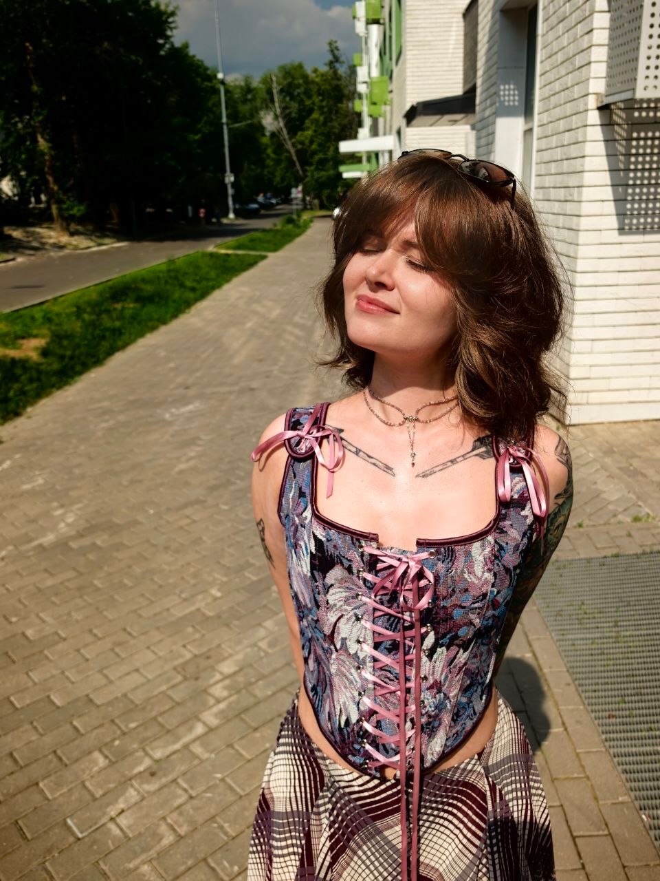 awondrr standing with eyes closed facing the sun wearing patterned corset top with pink lacing