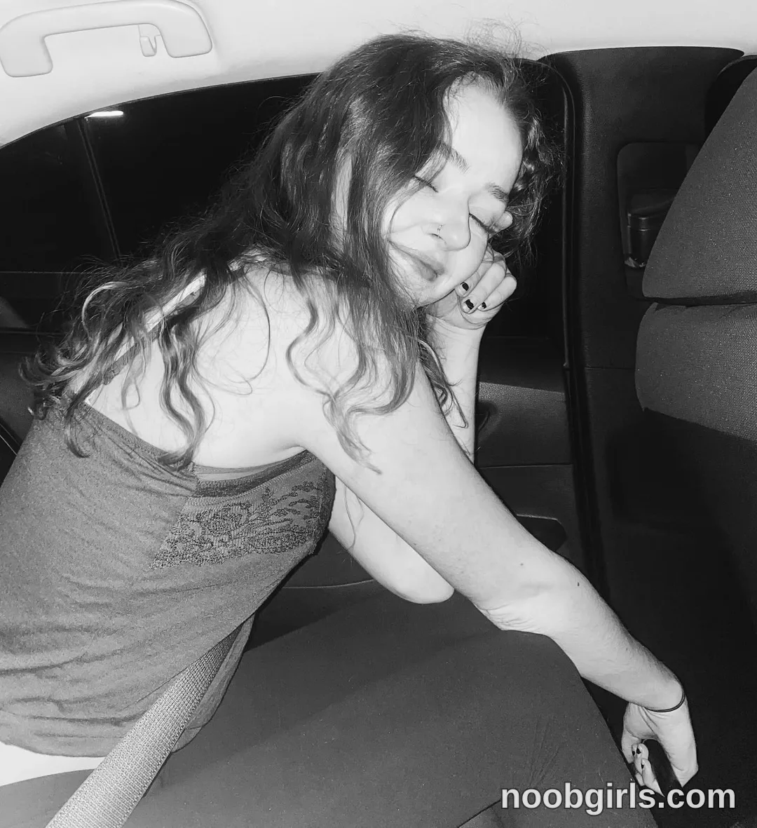 Britt sitting in a car with eyes closed wearing camisole top in car backseat