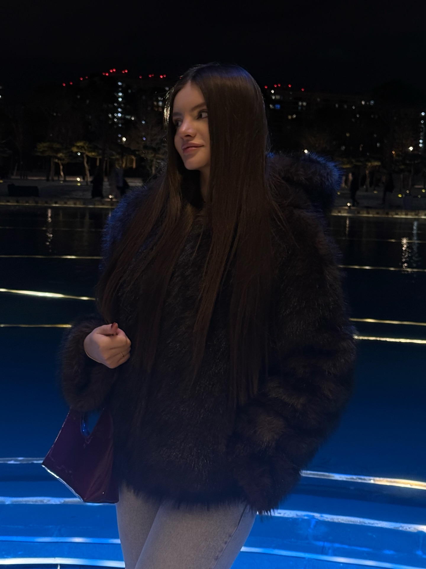 bellacle wearing dark fur coat in waterfront at night