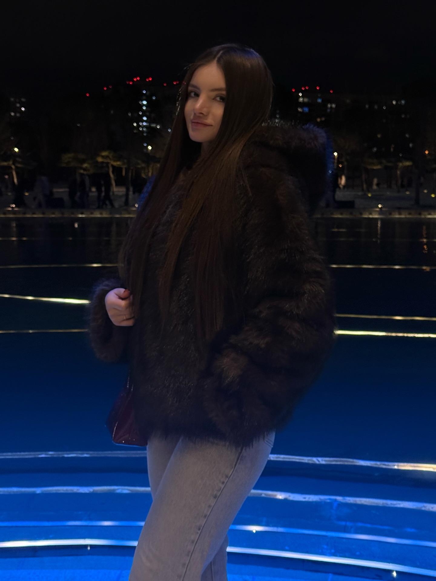 bellacle wearing dark fur jacket in illuminated plaza