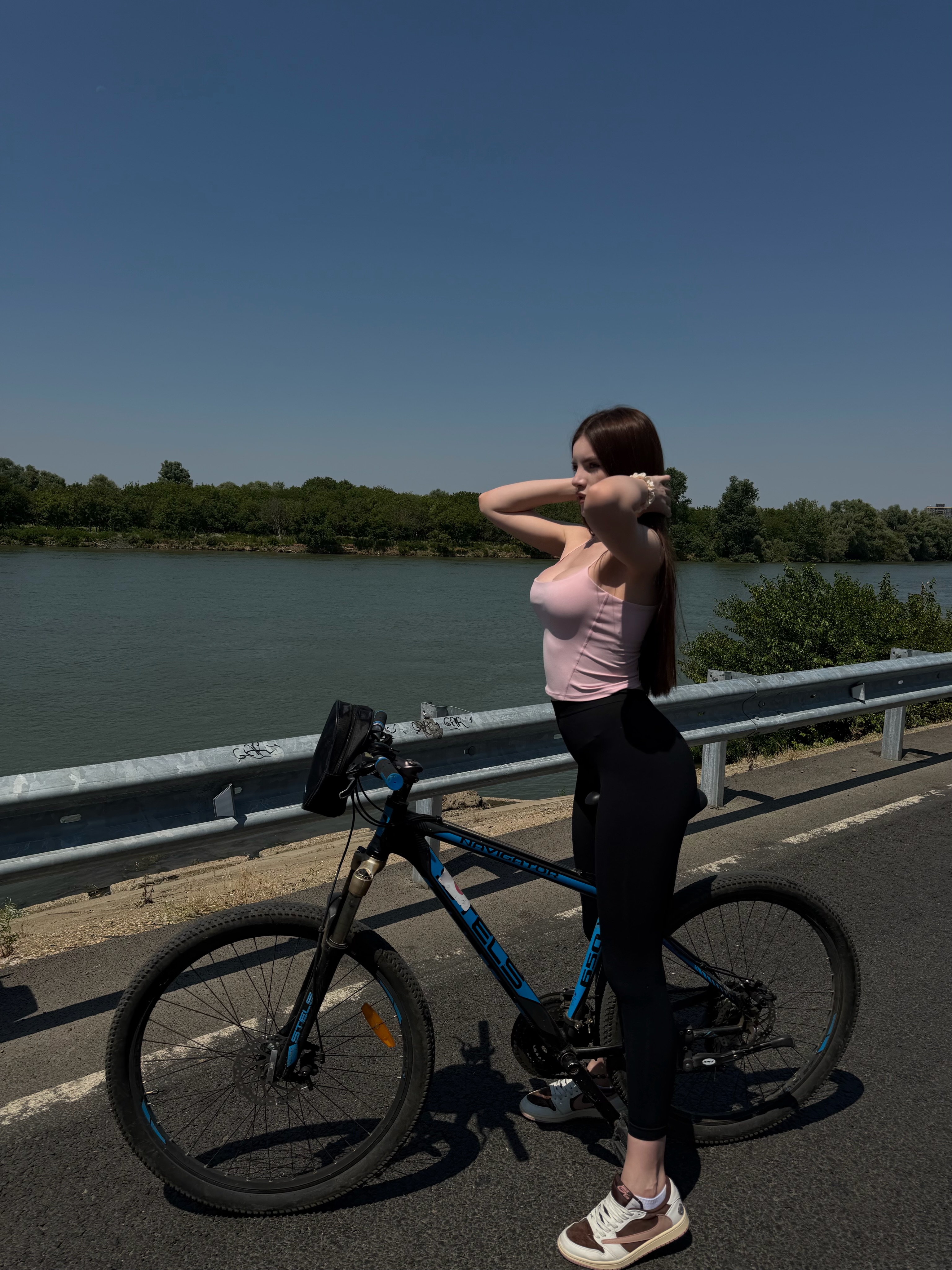bellacle standing with a bicycle wearing pink tank top in road beside river