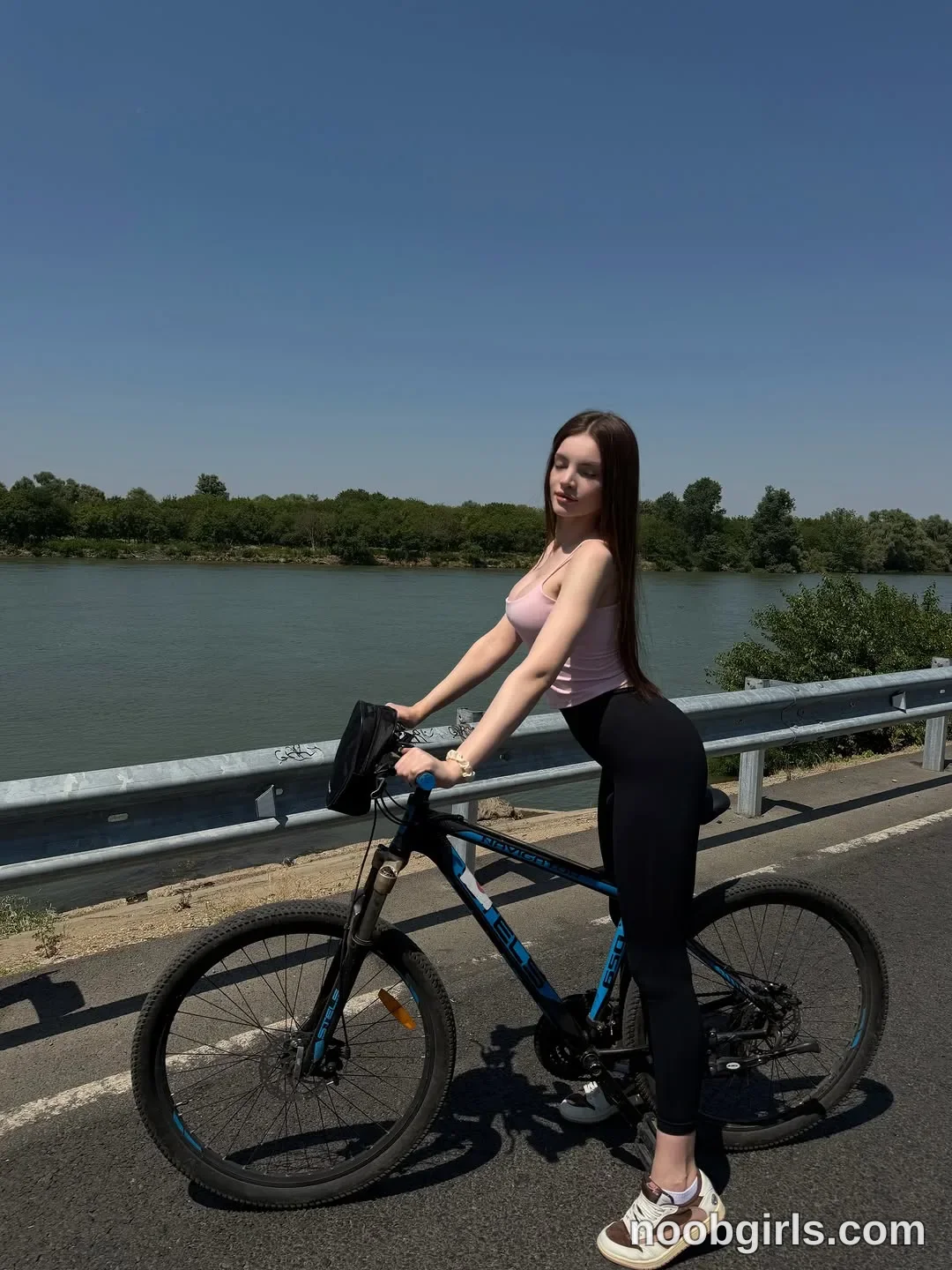 bellacle straddling a bicycle with one foot on the pedal wearing light pink spaghetti strap tank top
