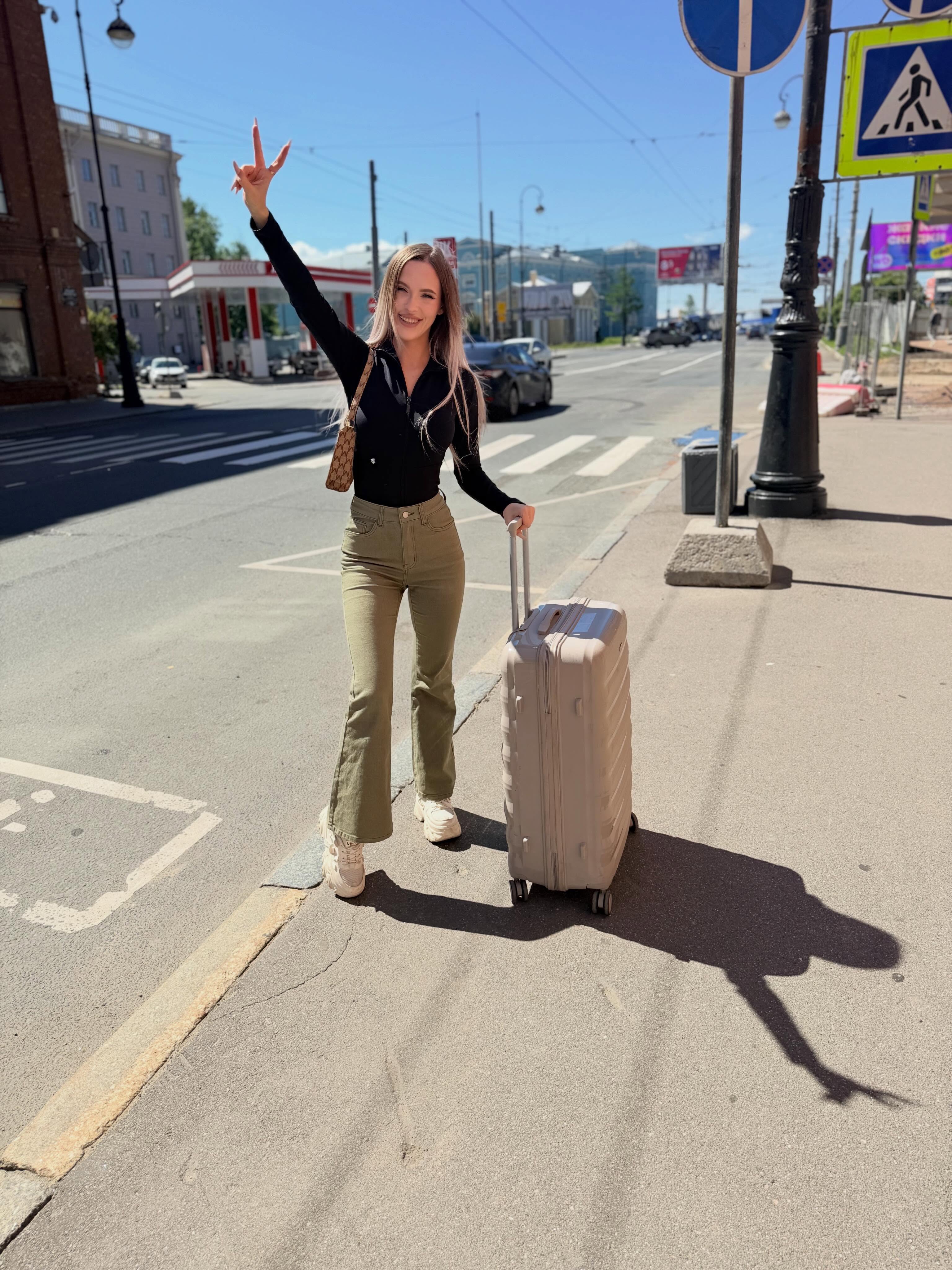 blush_mikki standing with a suitcase wearing black long-sleeve top in city sidewalk