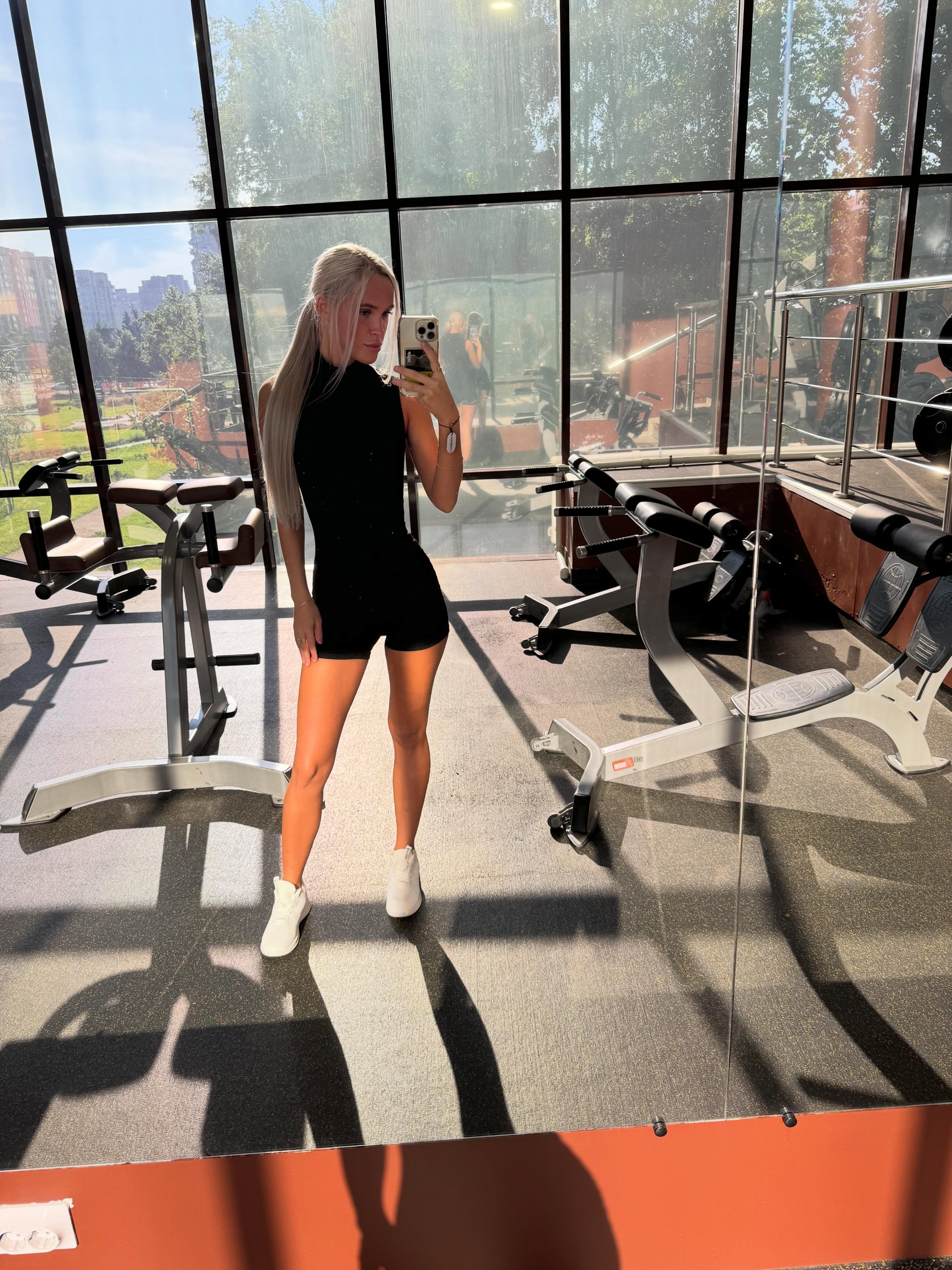 blush_mikki taking a mirror selfie wearing black sleeveless romper in gym