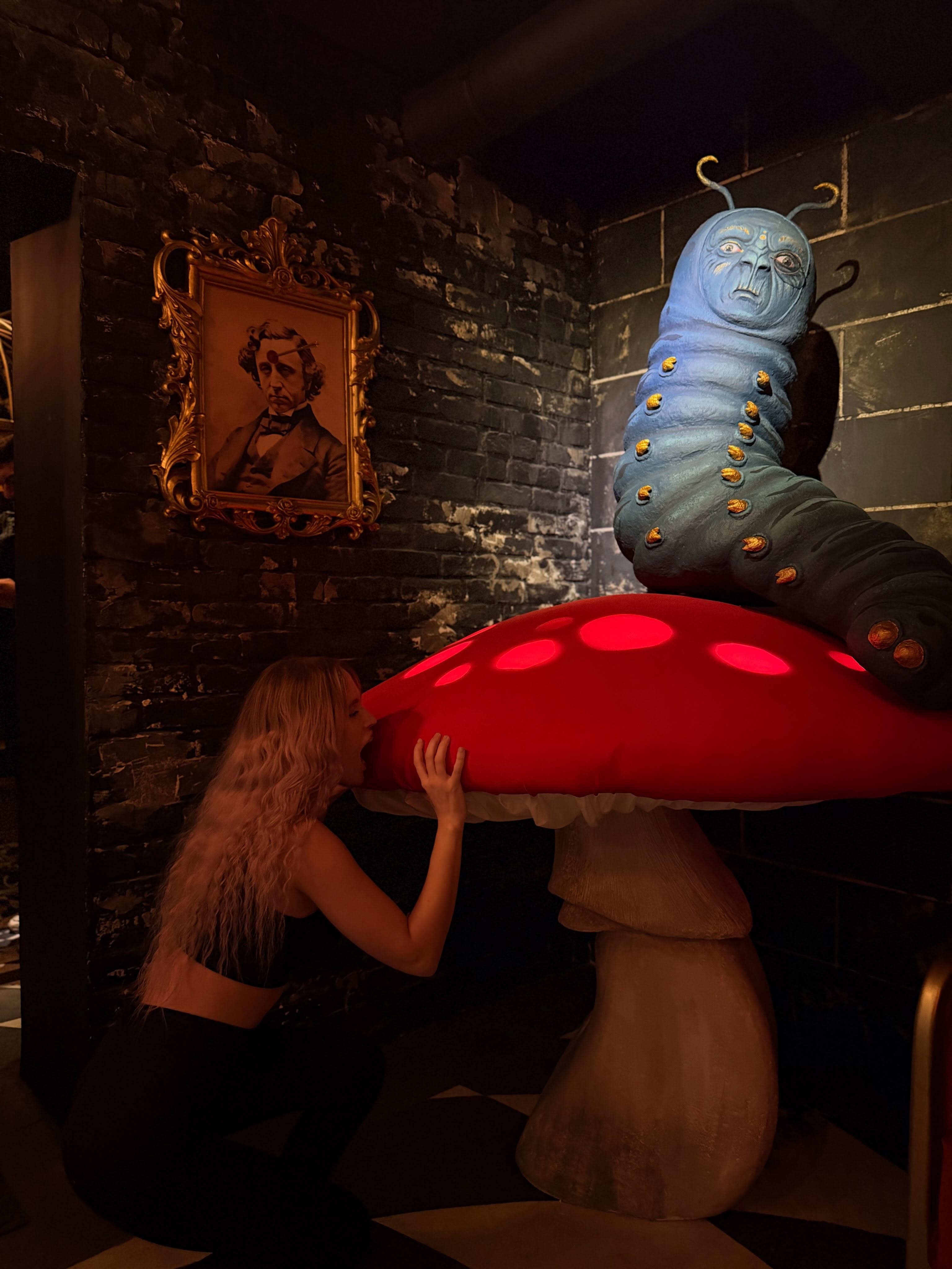 blush_mikki posing next to large mushroom sculpture wearing black crop top in themed indoor room