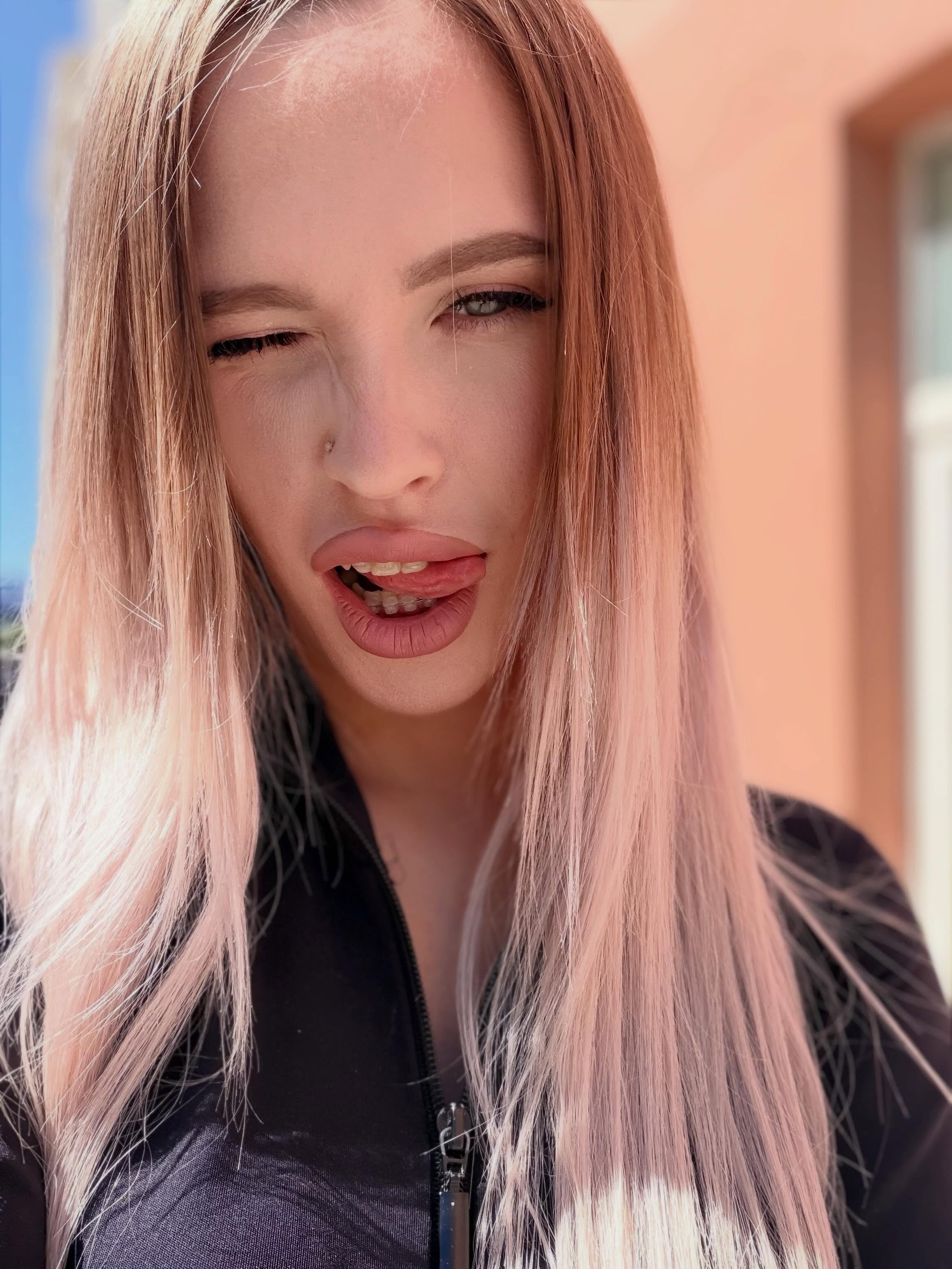 blush_mikki winking wearing black zip-up top by a building