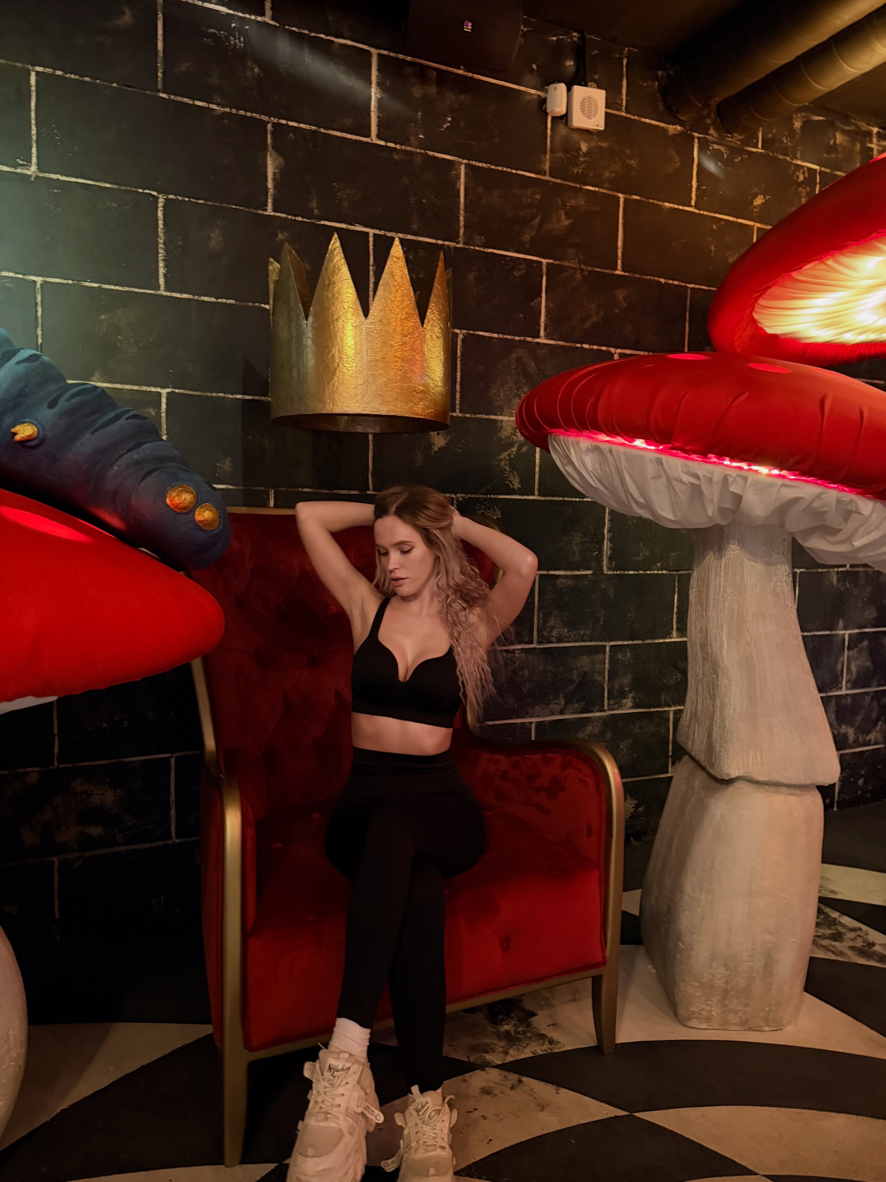 blush_mikki sitting on a red chair wearing black sports bra in themed indoor room