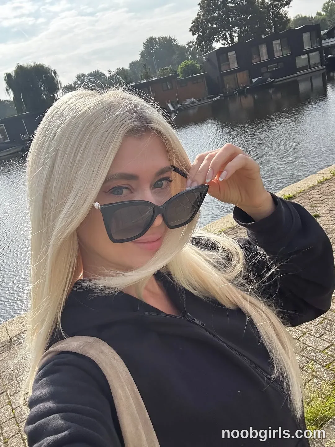 BunnyBlondyX facing the camera with one arm extended toward it wearing black zip-front jacket