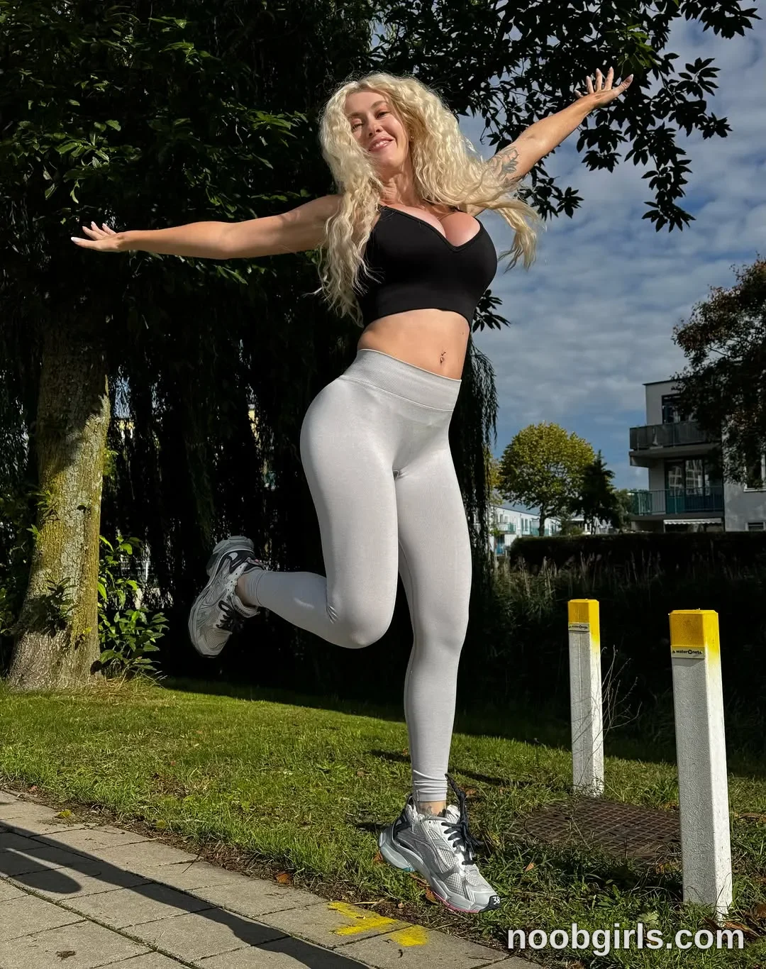 BunnyBlondyX airborne with both arms extended outward wearing Black sleeveless cropped top
